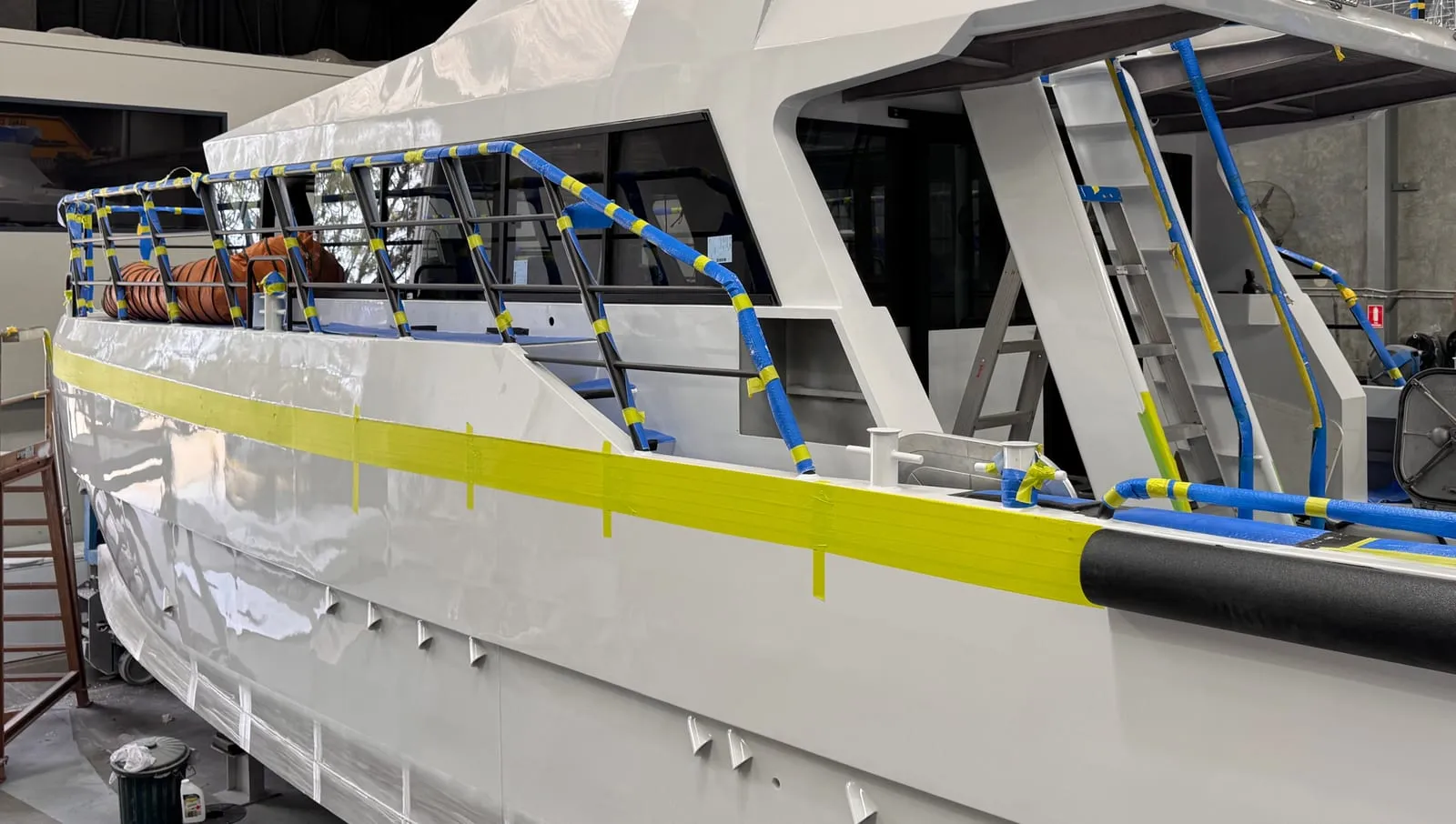 White aluminium workboat with its rails and hull stripe masked in blue and yellow tape before wrapping, in the Vinyl Wrapz workshop