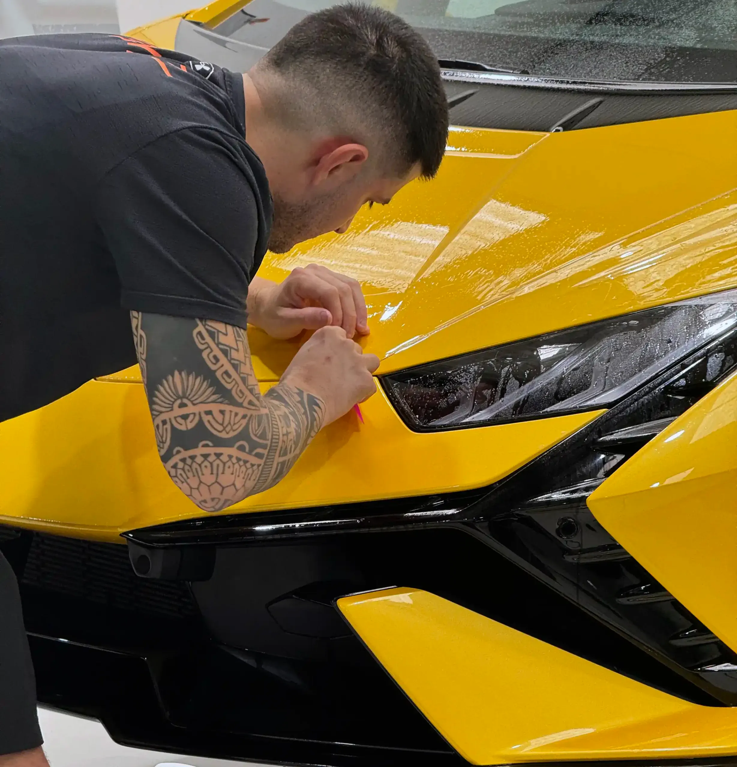 Installer fitting paint protection film around the headlight of a yellow Lamborghini Huracán at Vinyl Wrapz