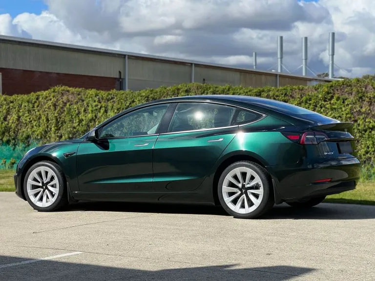 Tesla Model 3 in an iridescent green colour change wrap, rear three-quarter view