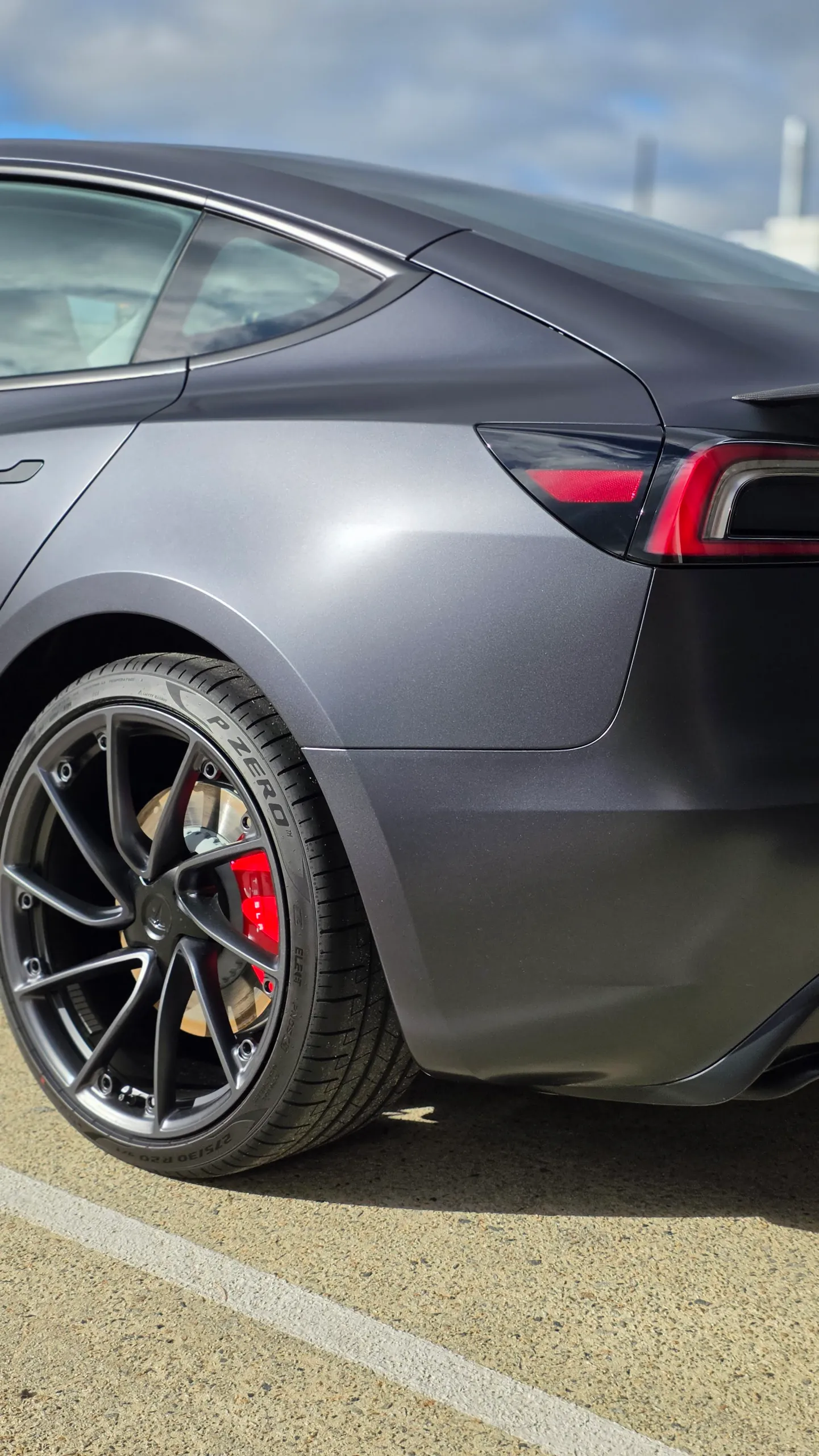 Tesla Model 3 rear light and wheel beneath matte dark grey bodywork outdoors