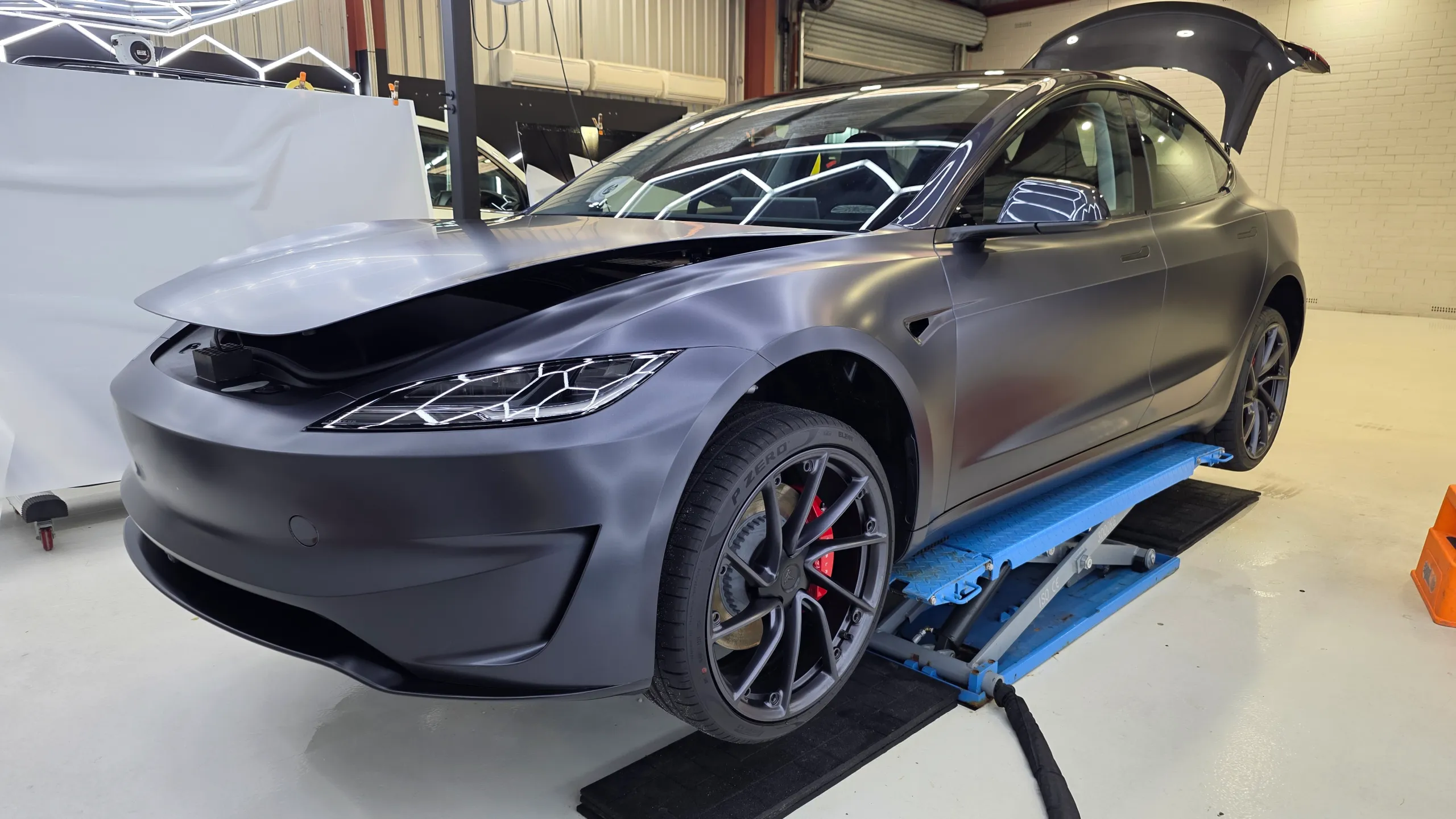 Satin grey Tesla Model 3 Performance on a workshop lift with its bonnet and boot open