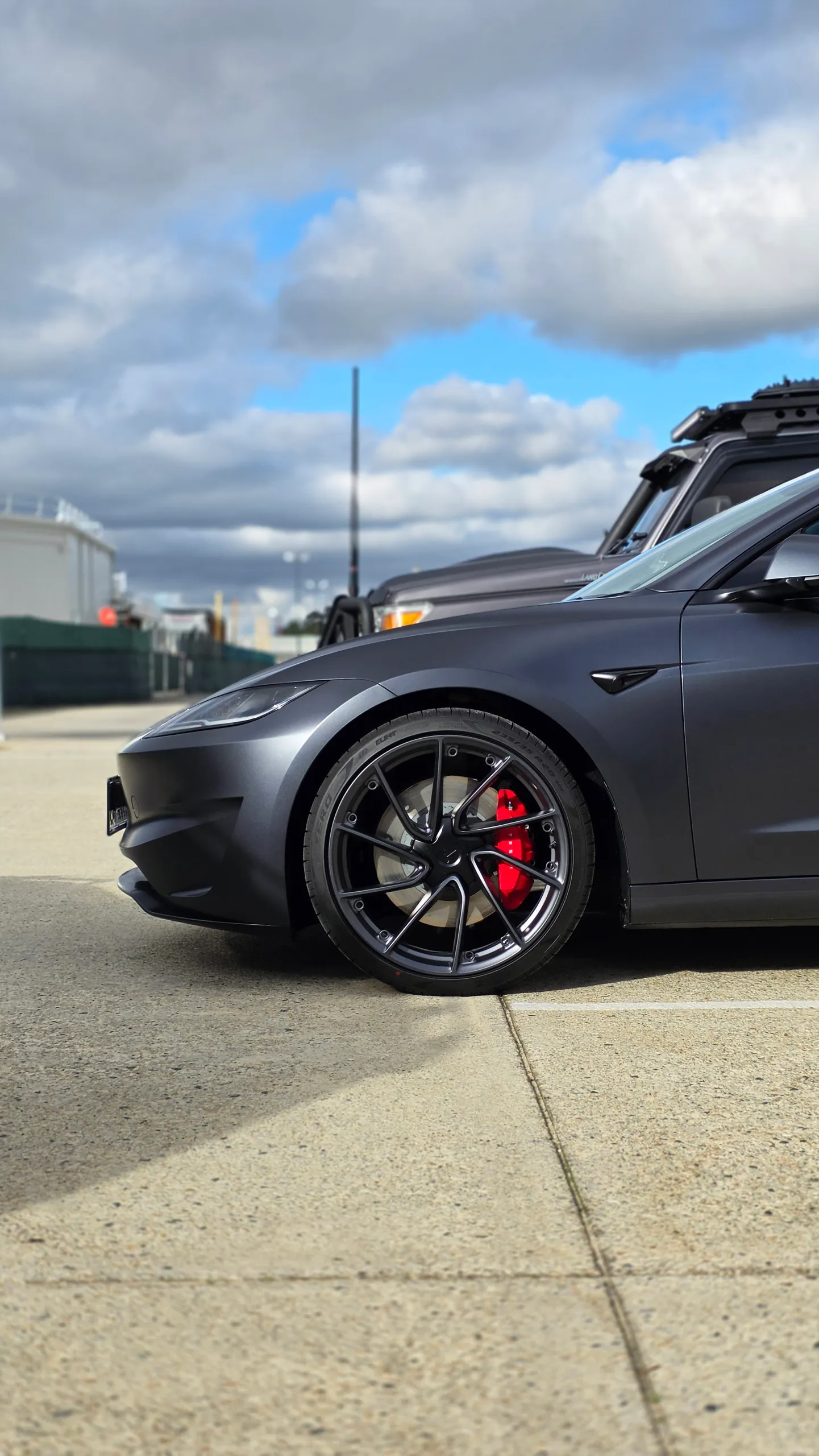 Tesla Model 3 front wheel and red brake caliper beneath a satin grey guard outdoors