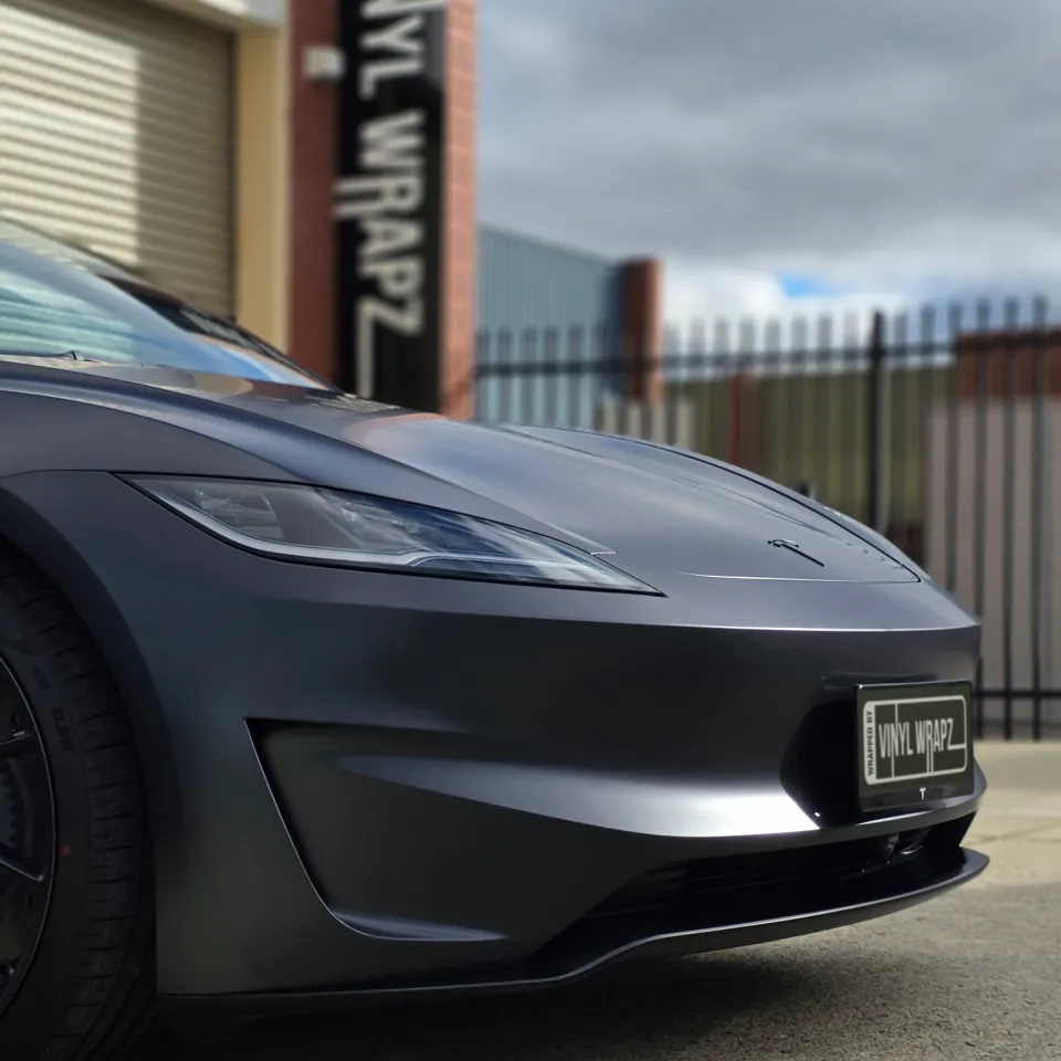 Low front-corner view of the satin grey Tesla Model 3 Performance outside the workshop