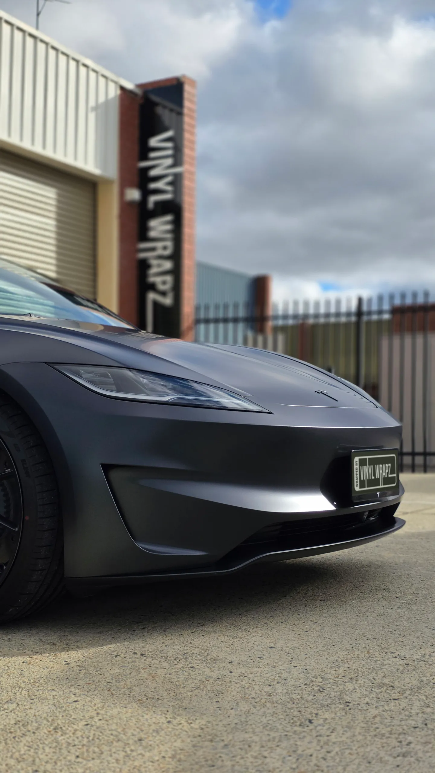 Low front-corner view of the satin grey Tesla Model 3 Performance outside the workshop
