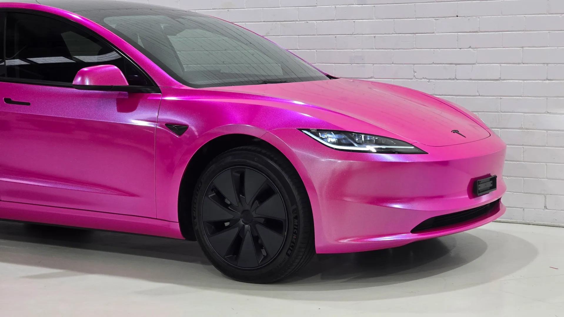 Gloss pink Tesla Model 3 front corner, wheel and headlight inside the workshop