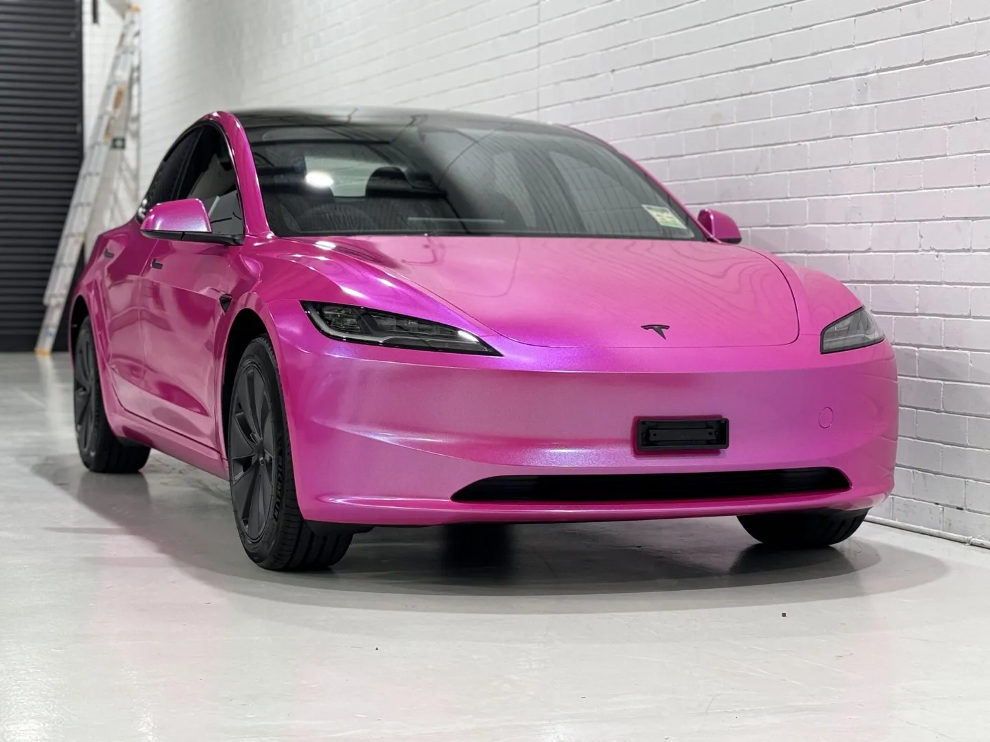 Front-quarter view of the gloss pink Tesla Model 3 inside the workshop