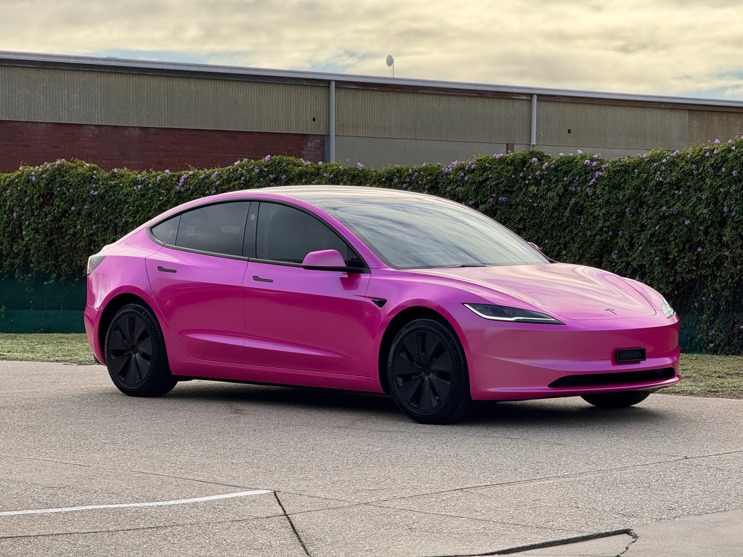 Gloss pink Tesla Model 3 viewed from the front quarter outside the workshop