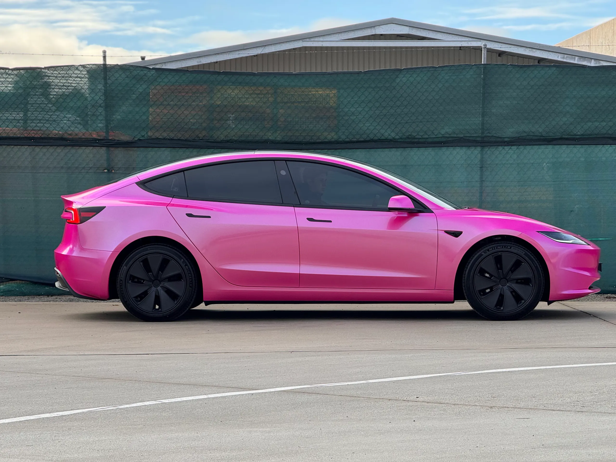 Side profile of the pink Tesla Model 3 with black wheels outdoors