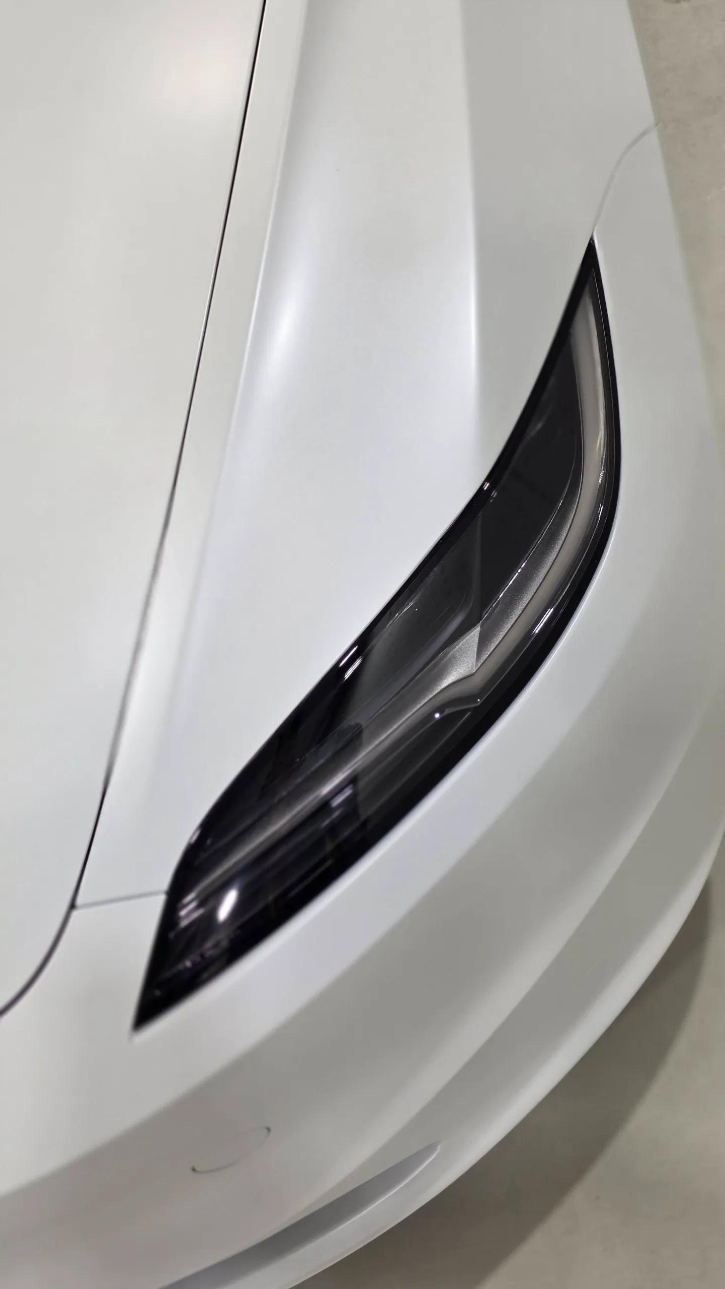 White Tesla Model 3 headlight and bonnet viewed from above