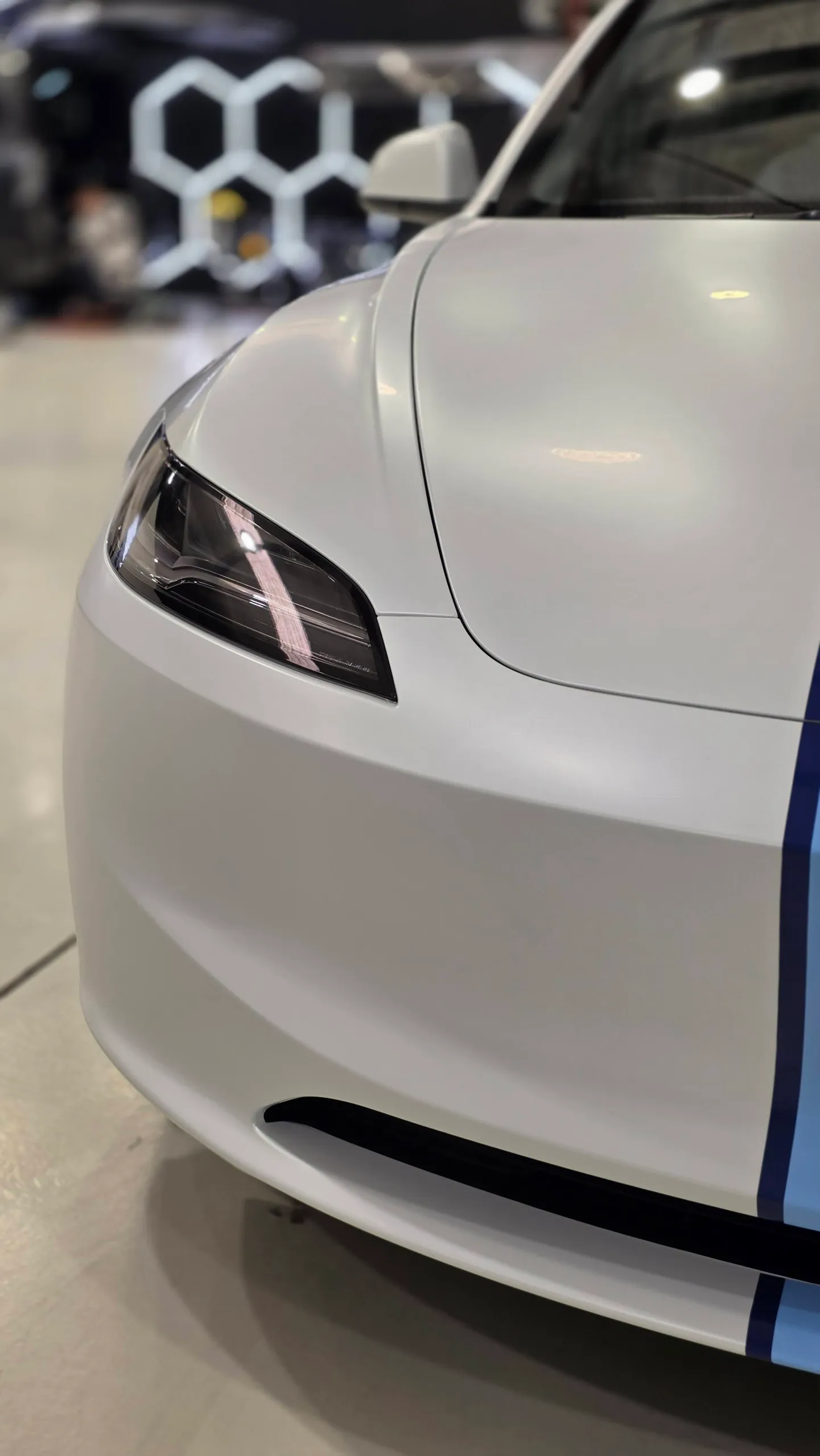 White Tesla front corner showing its slim headlight and bumper