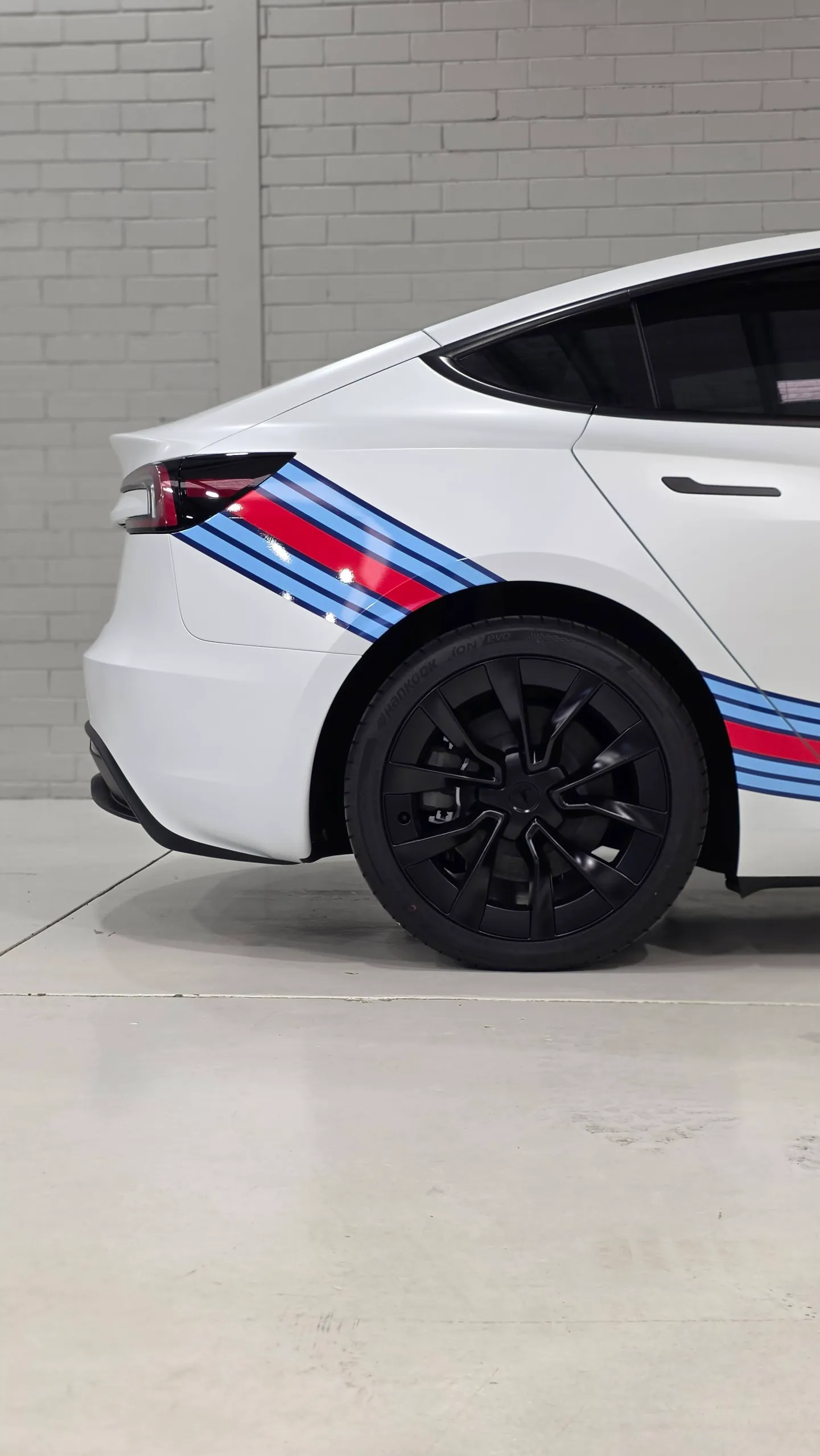 Cropped rear-quarter view of the white Tesla with Martini stripes inside the workshop