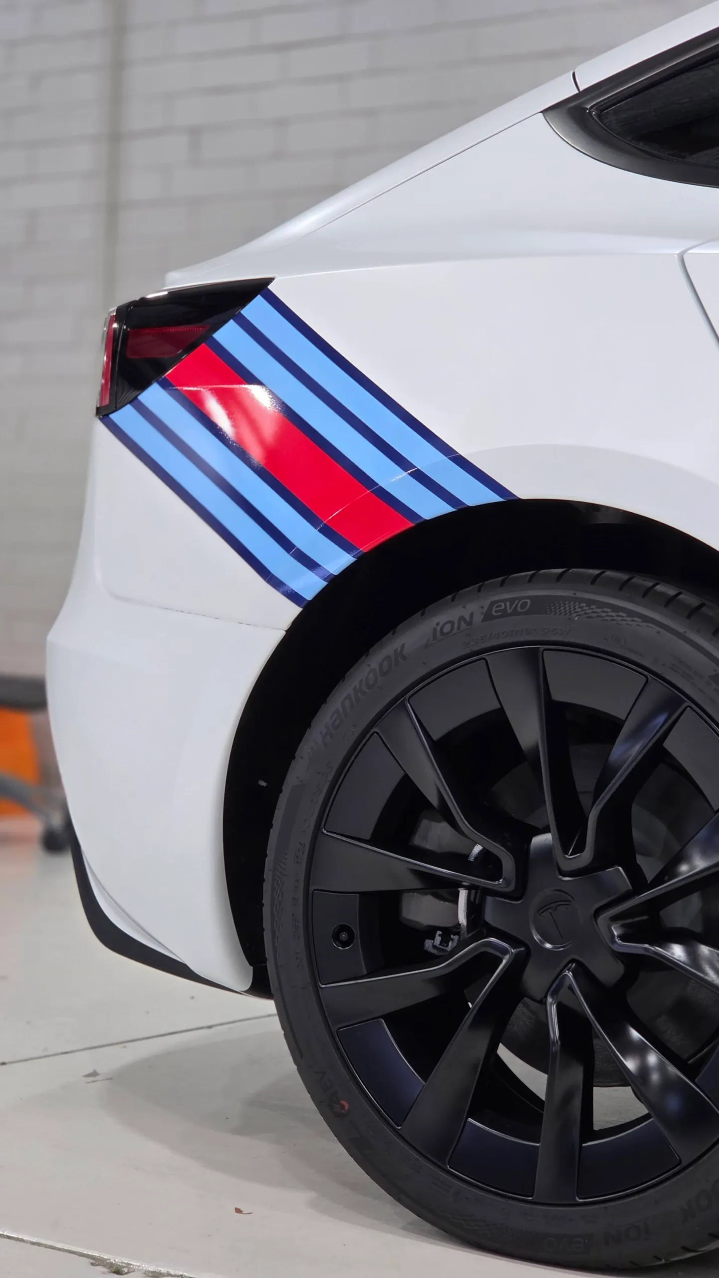 White Tesla rear quarter and black wheel above red and blue stripes