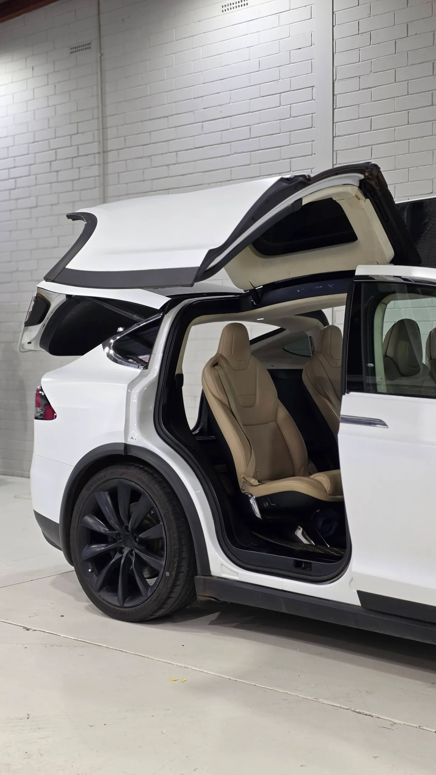Open falcon-wing door on a white Tesla Model X revealing its tan rear seats