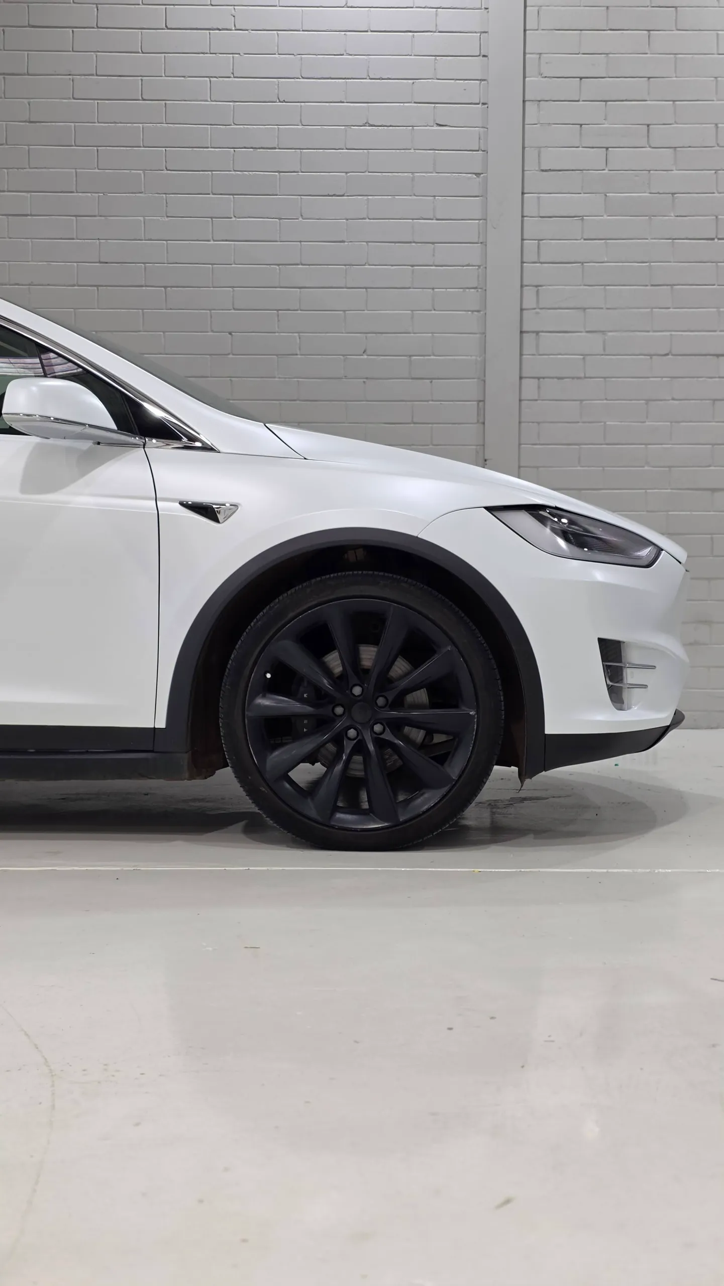 White Tesla Model X front wheel, guard and headlight inside the workshop