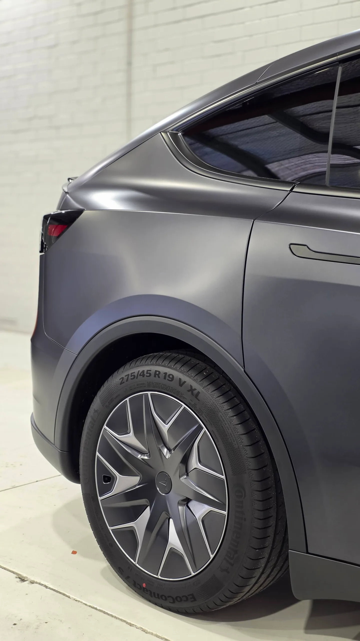Matte dark grey Tesla Model Y rear quarter and wheel in the workshop