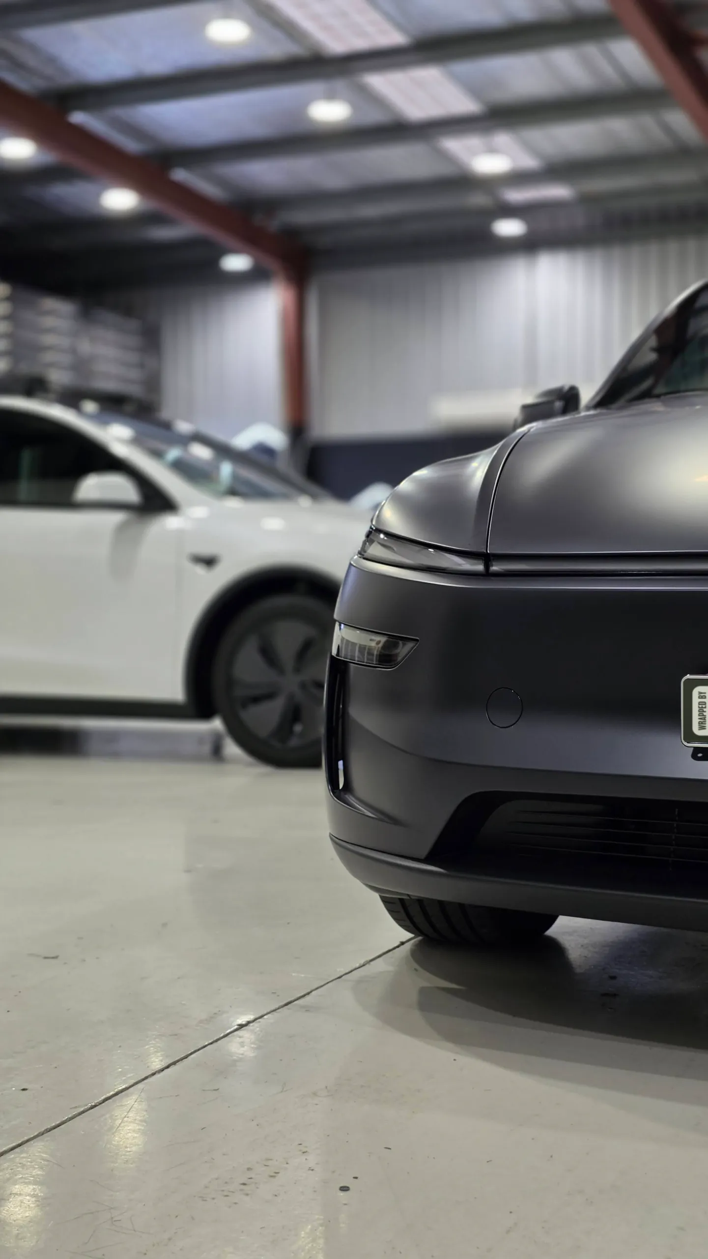 Cropped front corner of a matte dark grey Tesla Model Y in the workshop