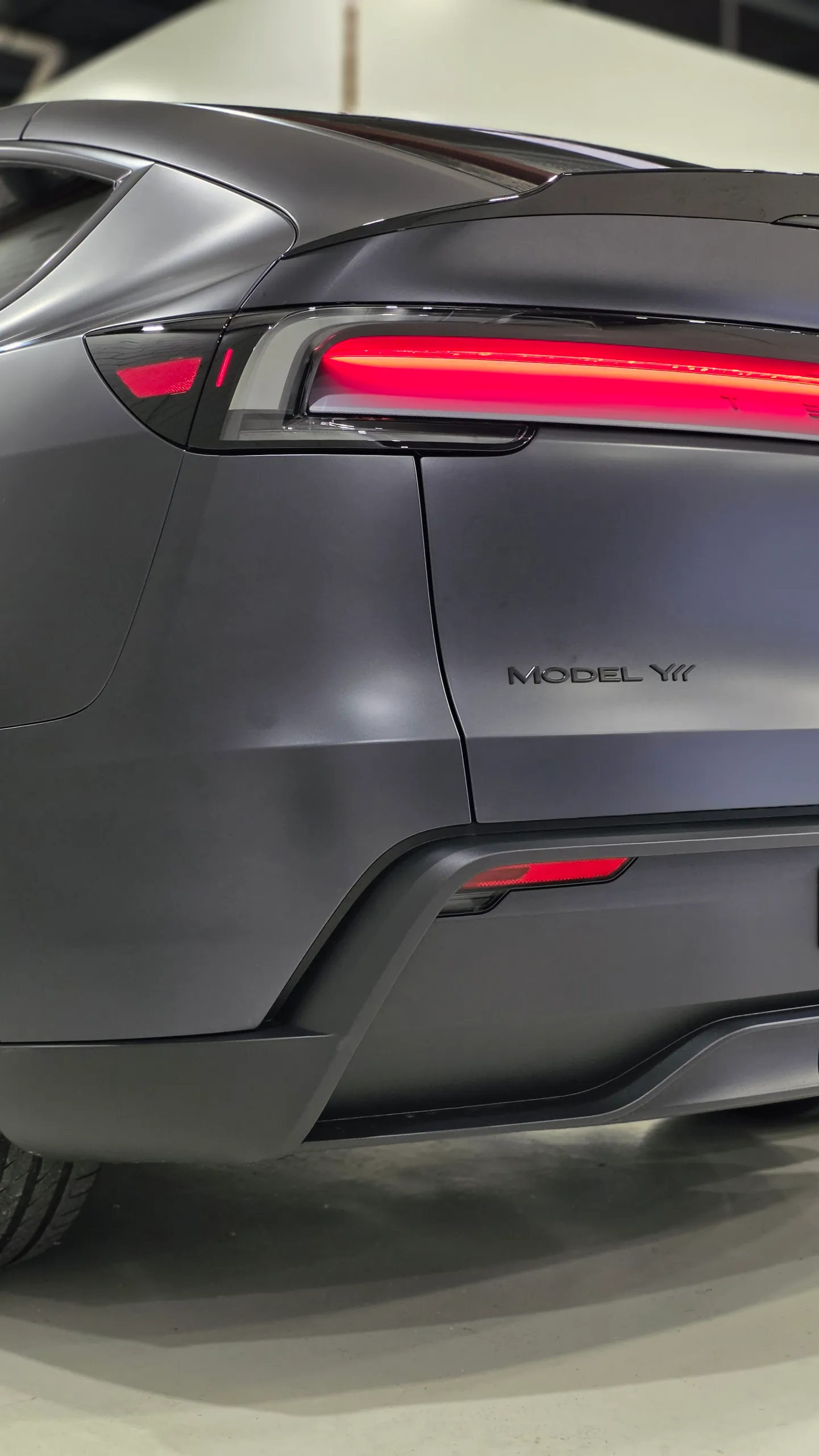 Matte dark grey Tesla Model Y rear light illuminated above the tailgate badge