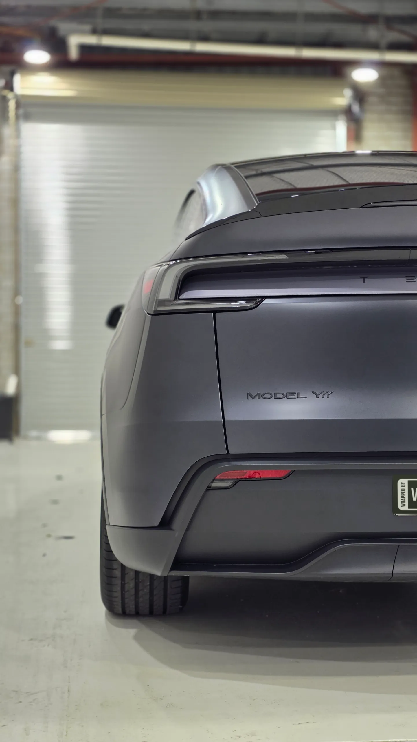 Cropped rear view of the matte dark grey Tesla Model Y with its light bar off