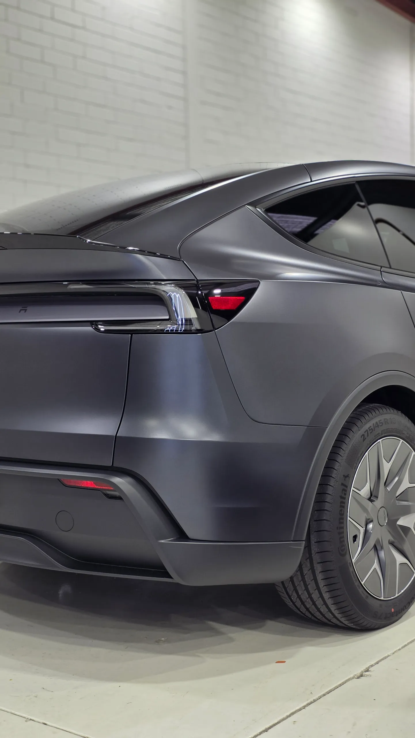 Rear-quarter detail of a matte dark grey Tesla Model Y showing its tailgate, bumper and rear wheel