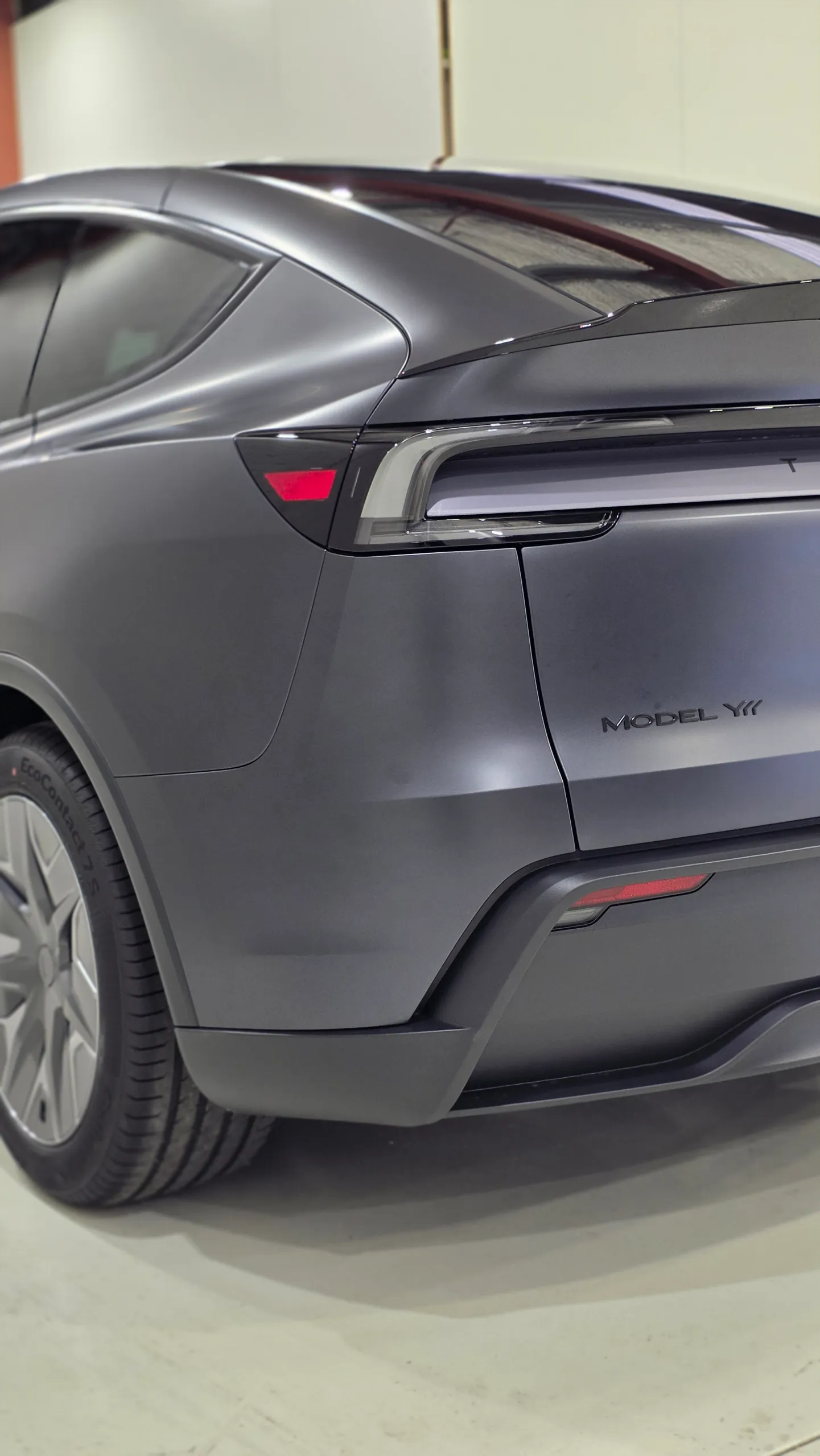 Tesla Model Y rear corner with a matte dark grey finish and unlit rear light bar