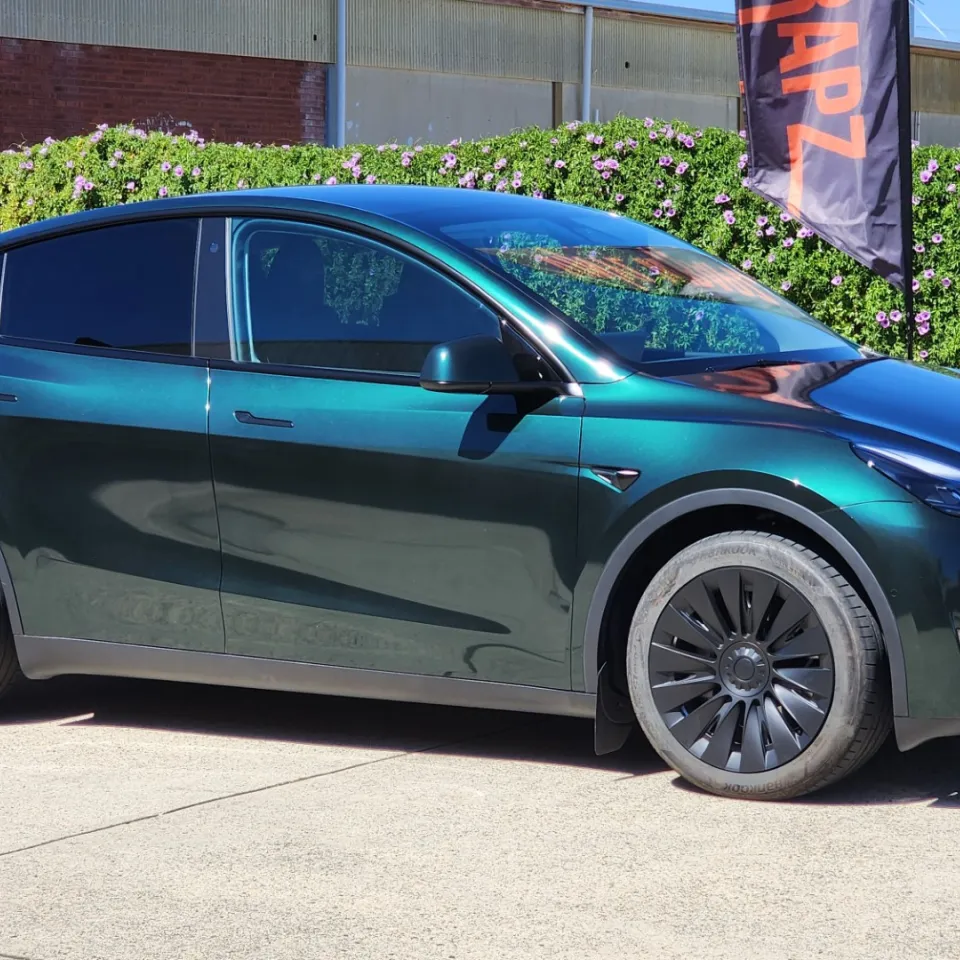 Tesla Model Y with a gloss green-black iridescent finish outside the workshop