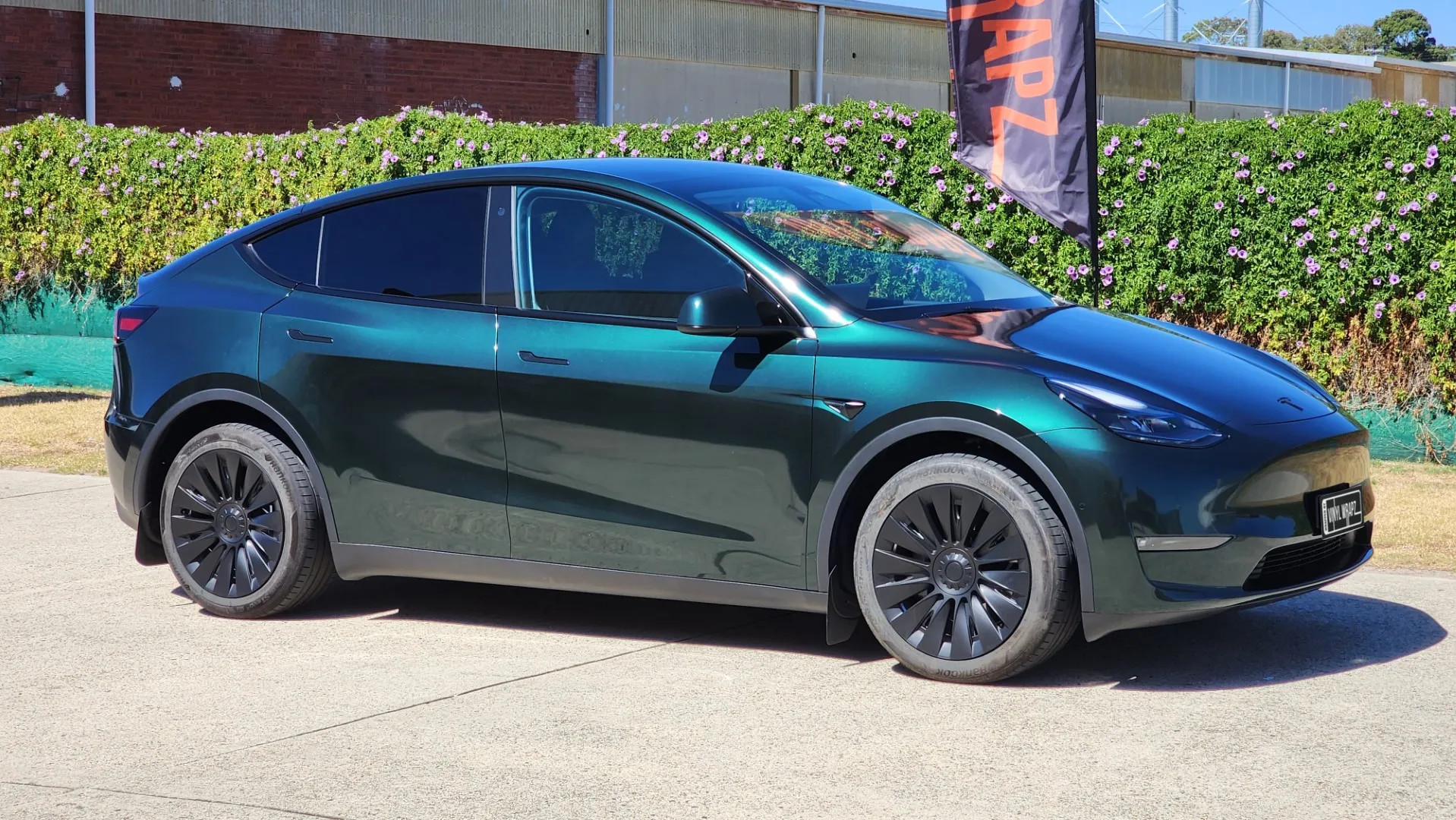 Tesla Model Y with a gloss green-black iridescent finish outside the workshop