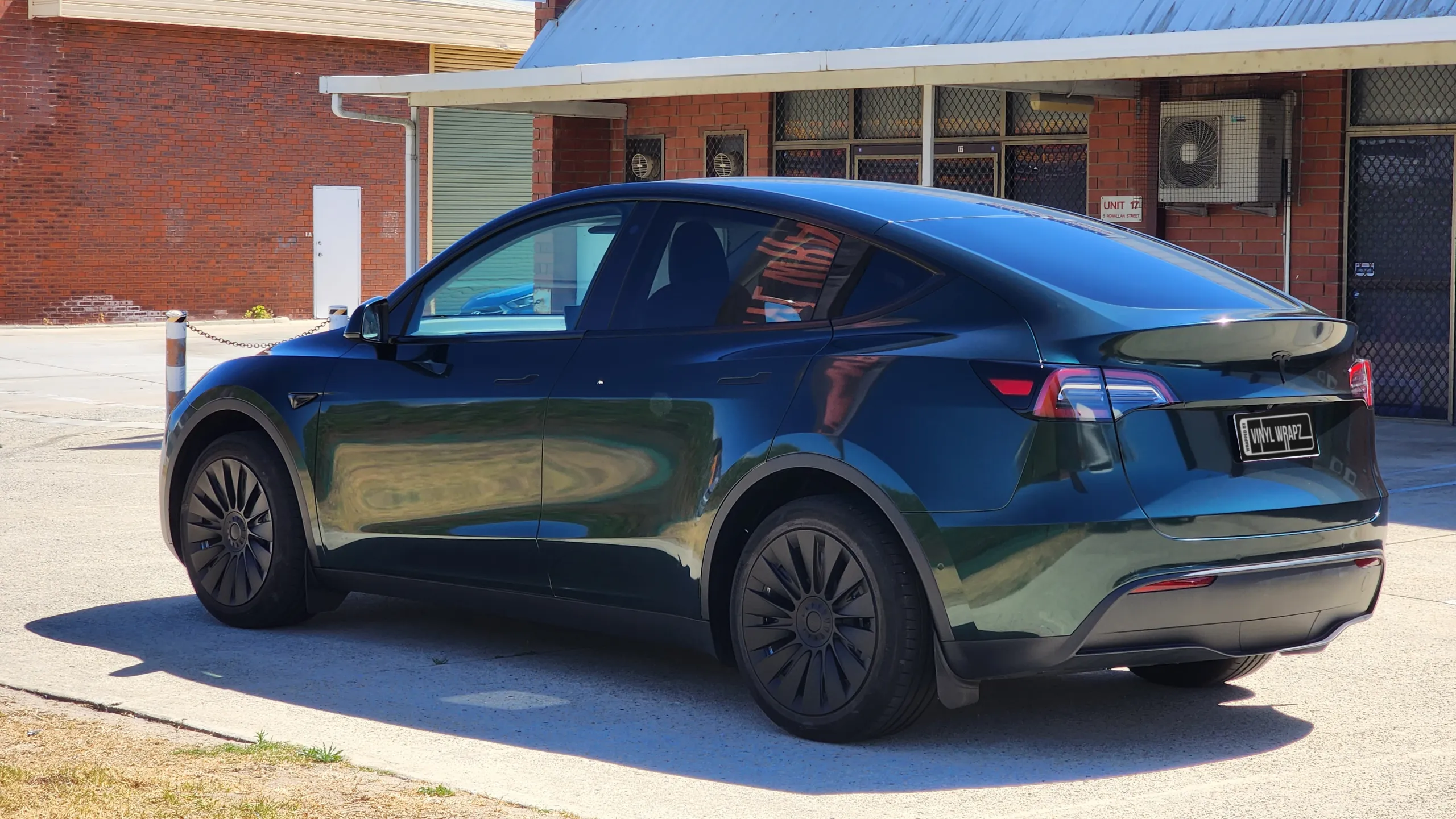 Gloss green and black iridescent Tesla Model Y outside the workshop, rear quarter