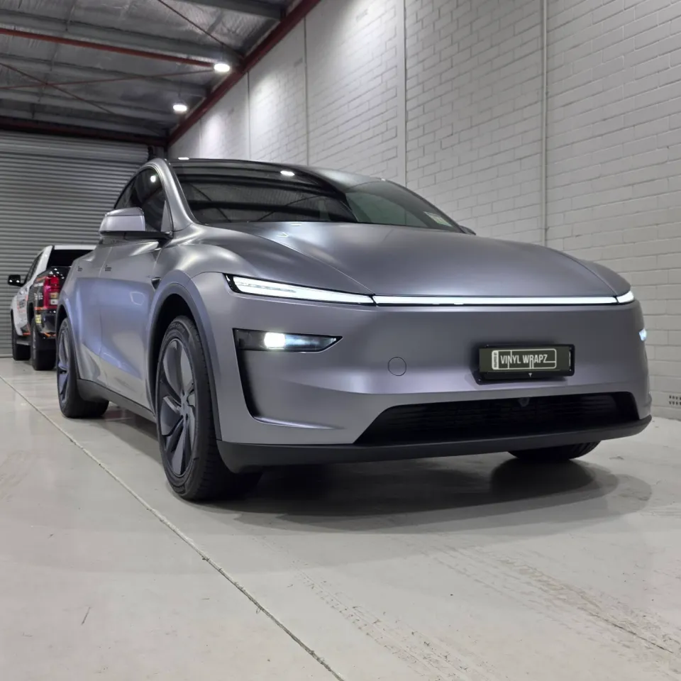 Satin grey Tesla Model Y with its front lights illuminated in the workshop