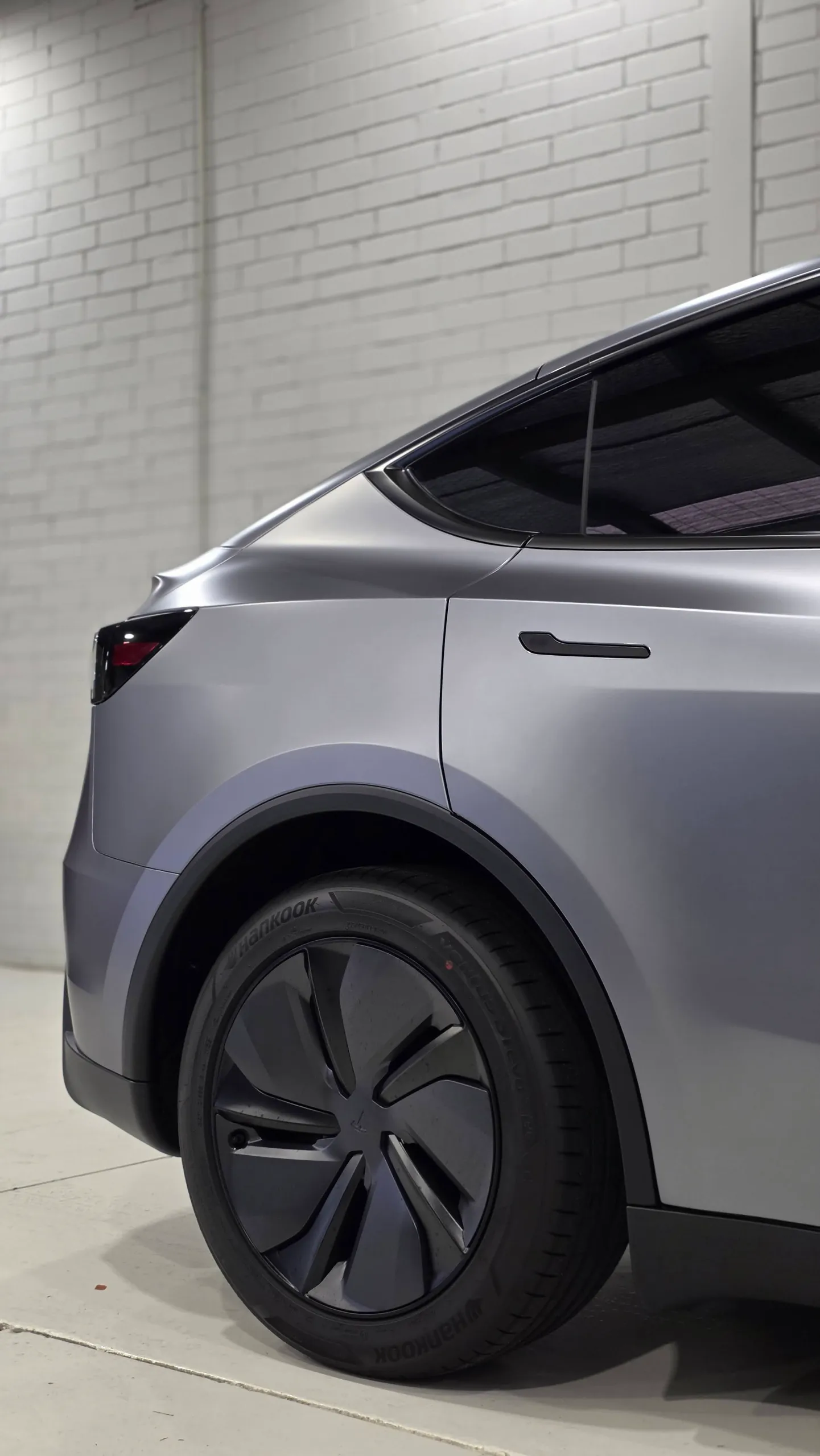 Satin grey Tesla Model Y rear wheel and rear door against a white workshop wall