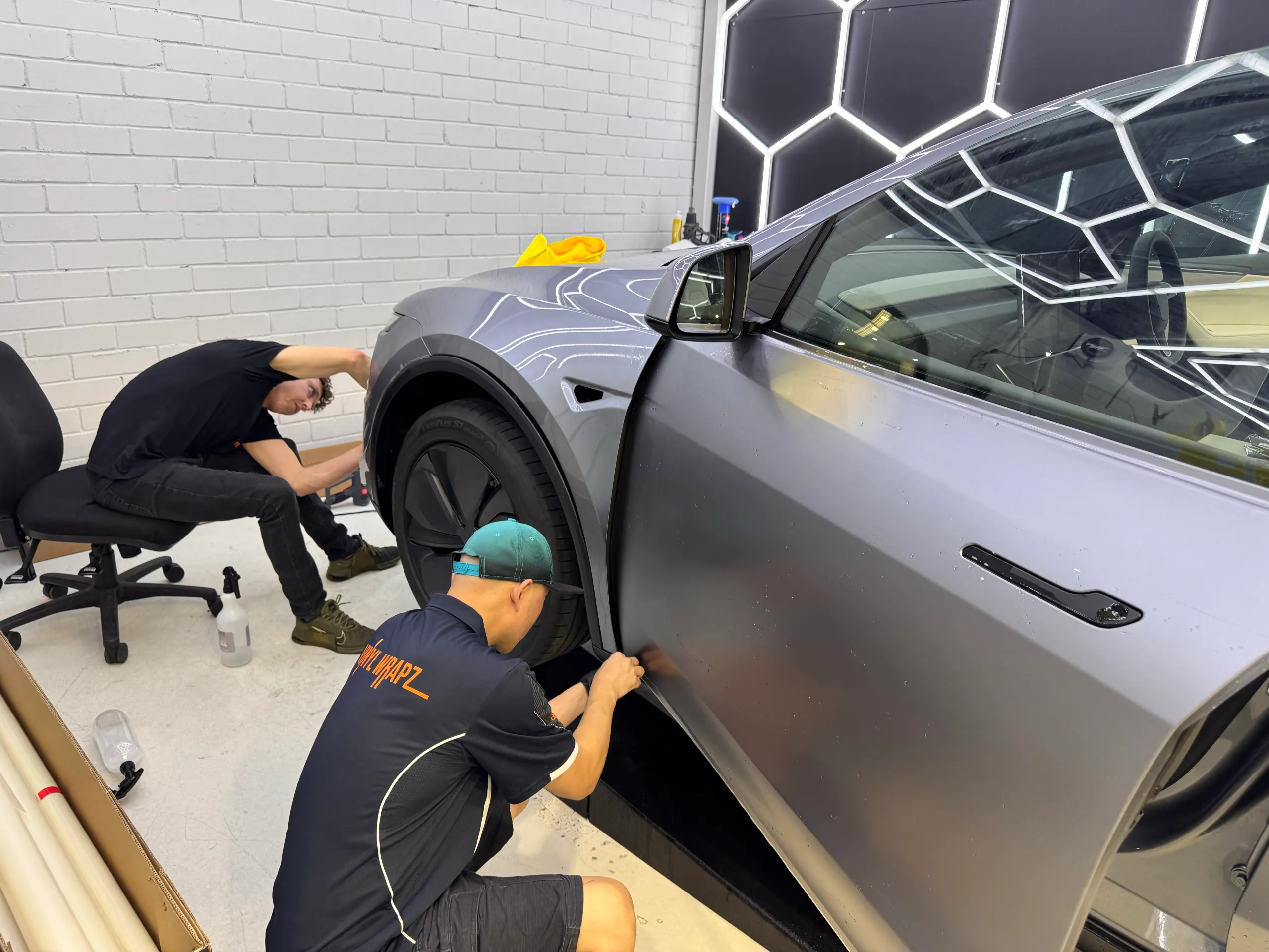 Two installers working on the Tesla Model Y front guard and door during film installation
