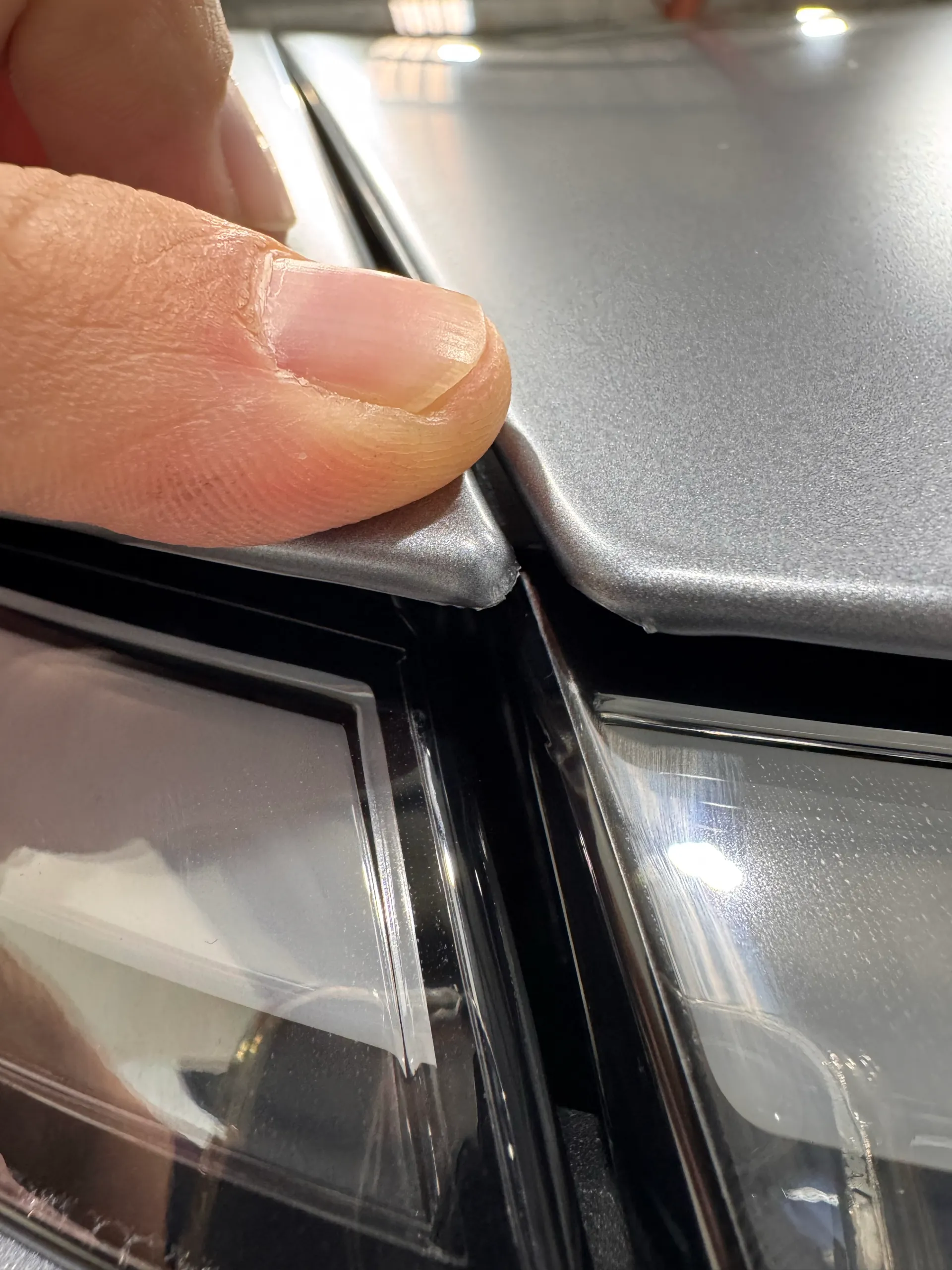 A finger indicating the film edge above the Tesla Model Y front light bar