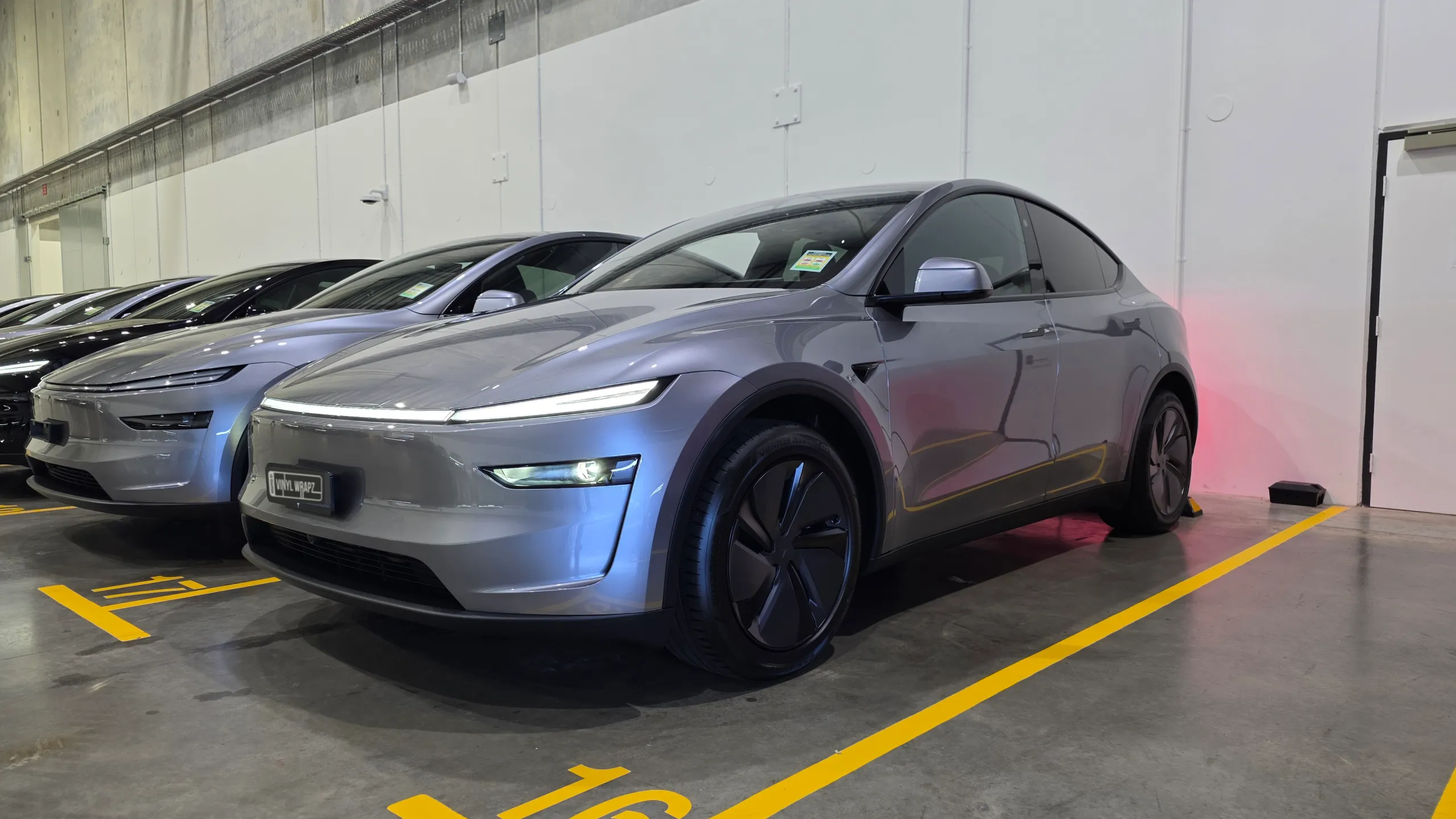 Gloss grey Tesla Model Y parked alongside other vehicles in an indoor parking area