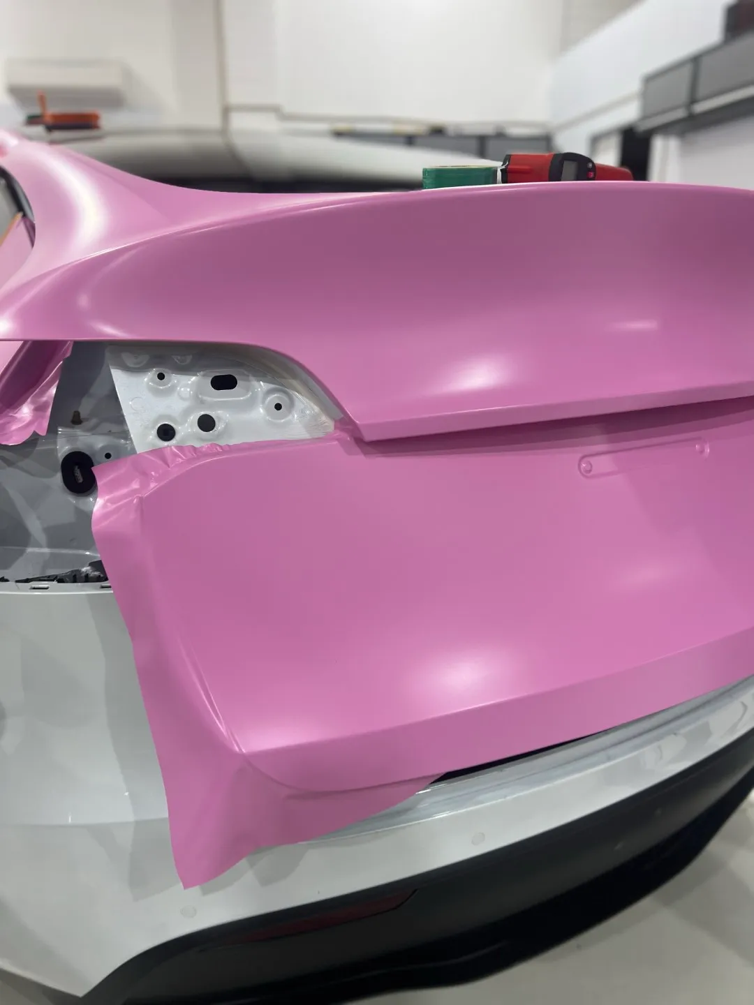 Pink film being fitted to the Tesla Model Y tailgate with the rear light removed