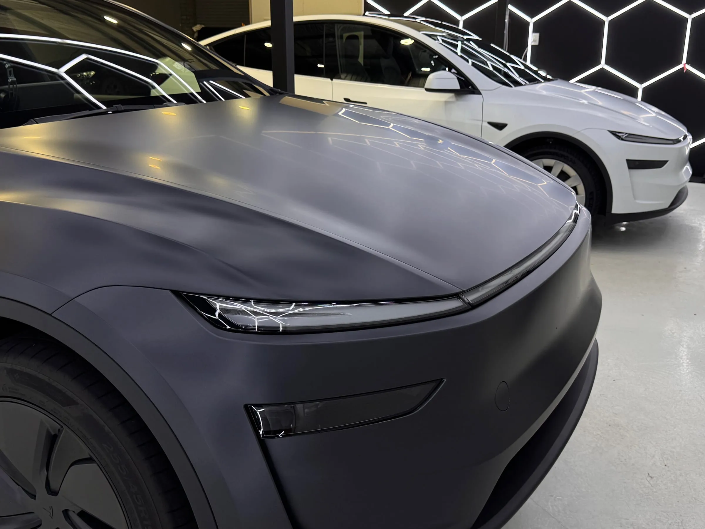 Satin grey paint protection film on the bonnet and headlight of a Tesla Model Y, a white Model Y behind it, Osborne Park