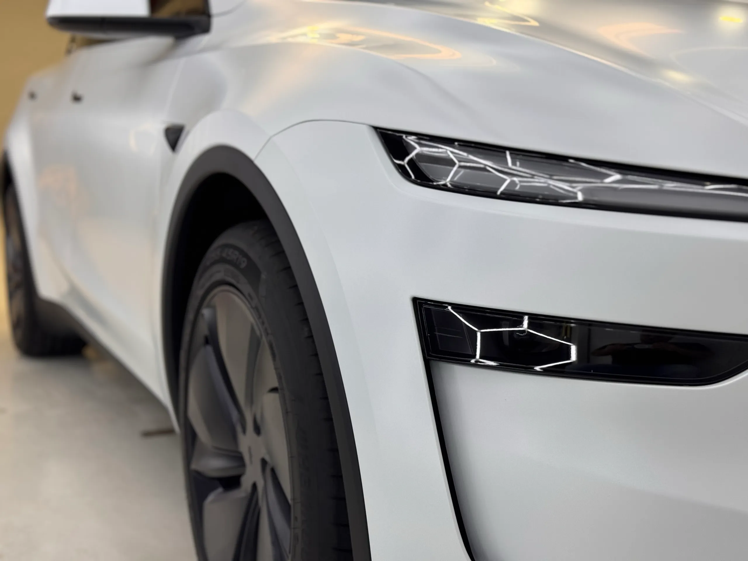 Close view of the white Tesla Model Y front wheel, light bar and lower headlight