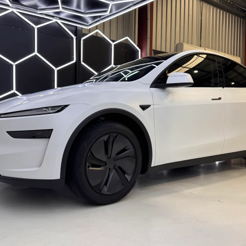Matte white Tesla Model Y viewed from the front quarter beneath workshop lights