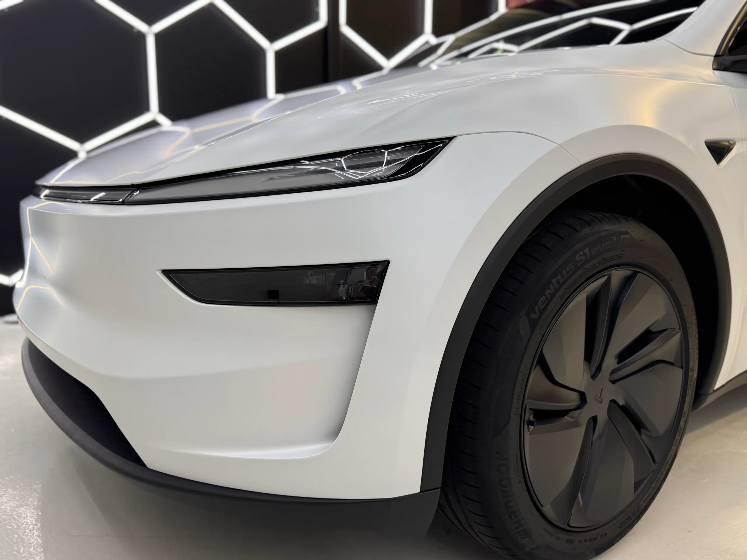 White Tesla Model Y front corner and dark wheel beneath its matte bonnet