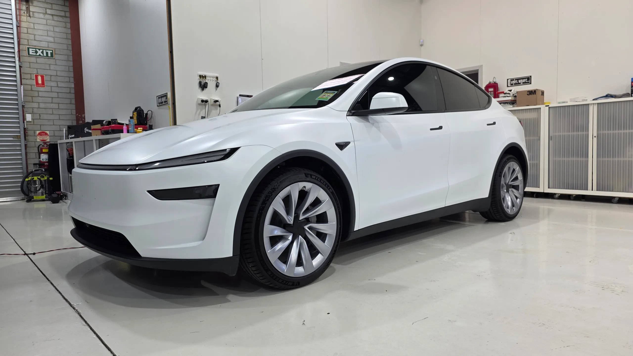 Satin white Tesla Model Y viewed from the front quarter in the workshop