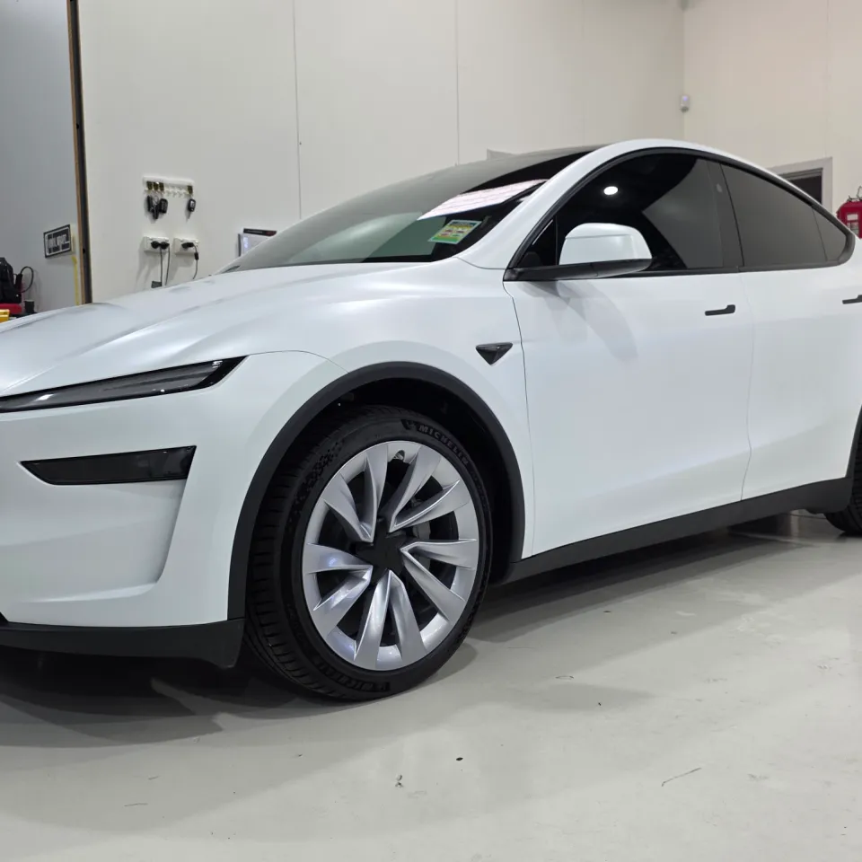 Satin white Tesla Model Y viewed from the front quarter in the workshop