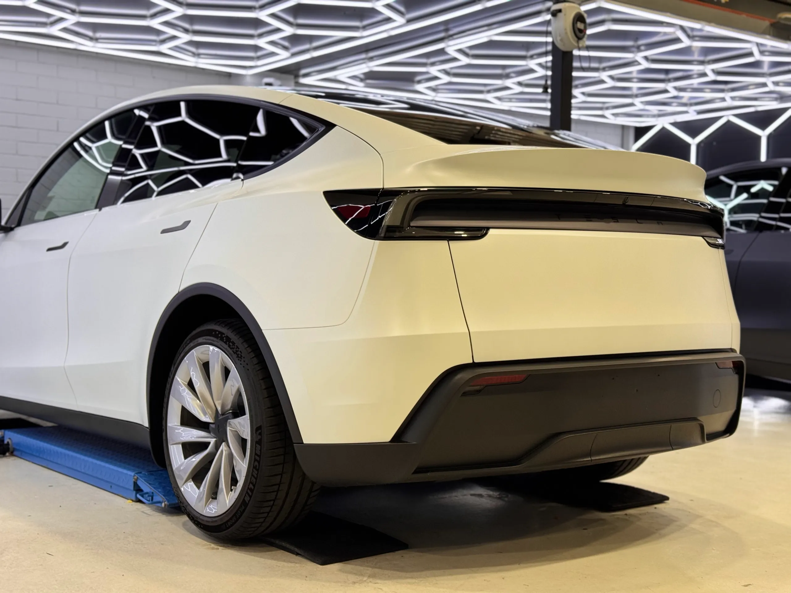 Rear-quarter view of the satin white Tesla Model Y on a workshop lift