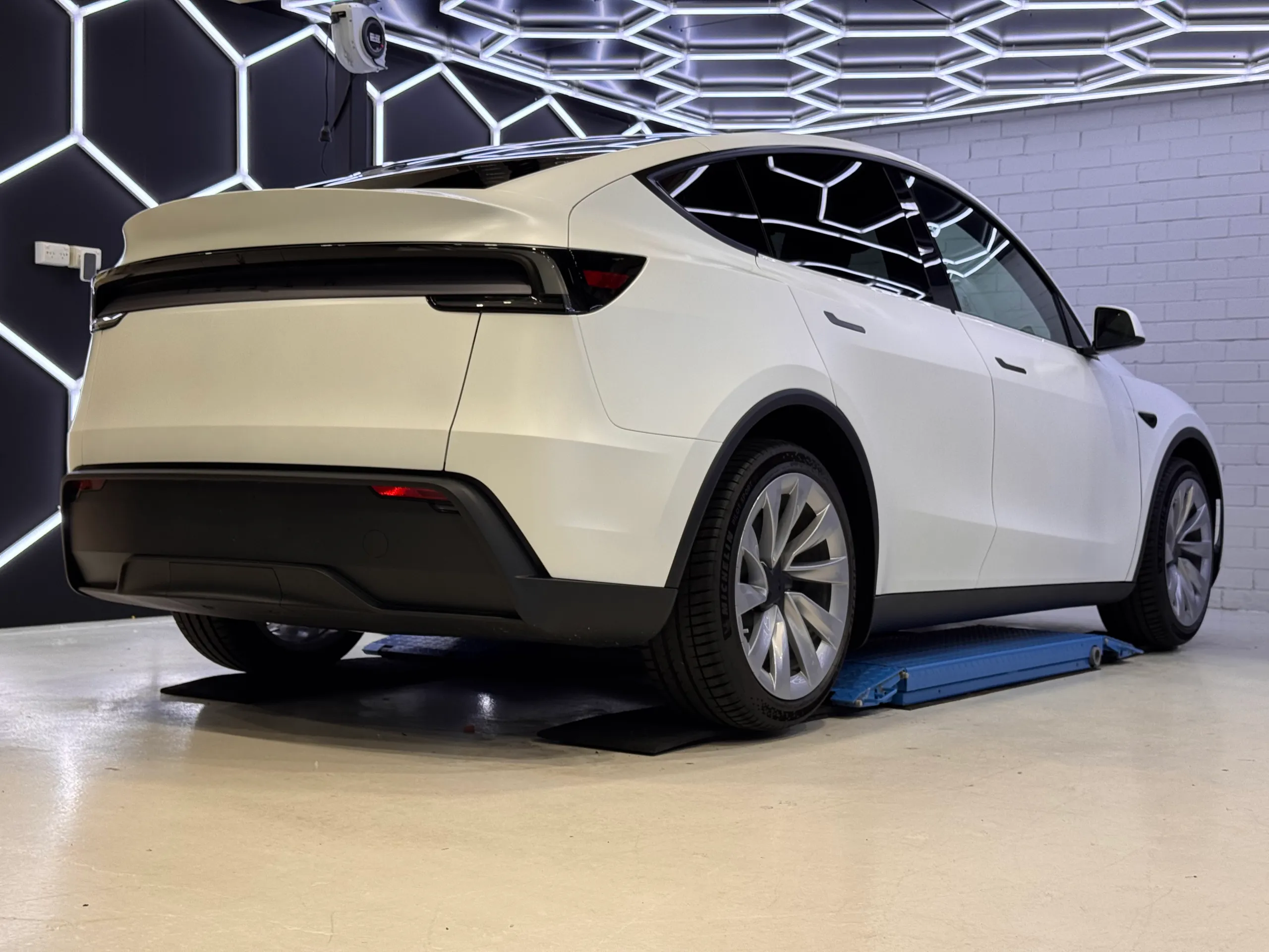 Low rear-quarter view of the satin white Tesla Model Y in the workshop