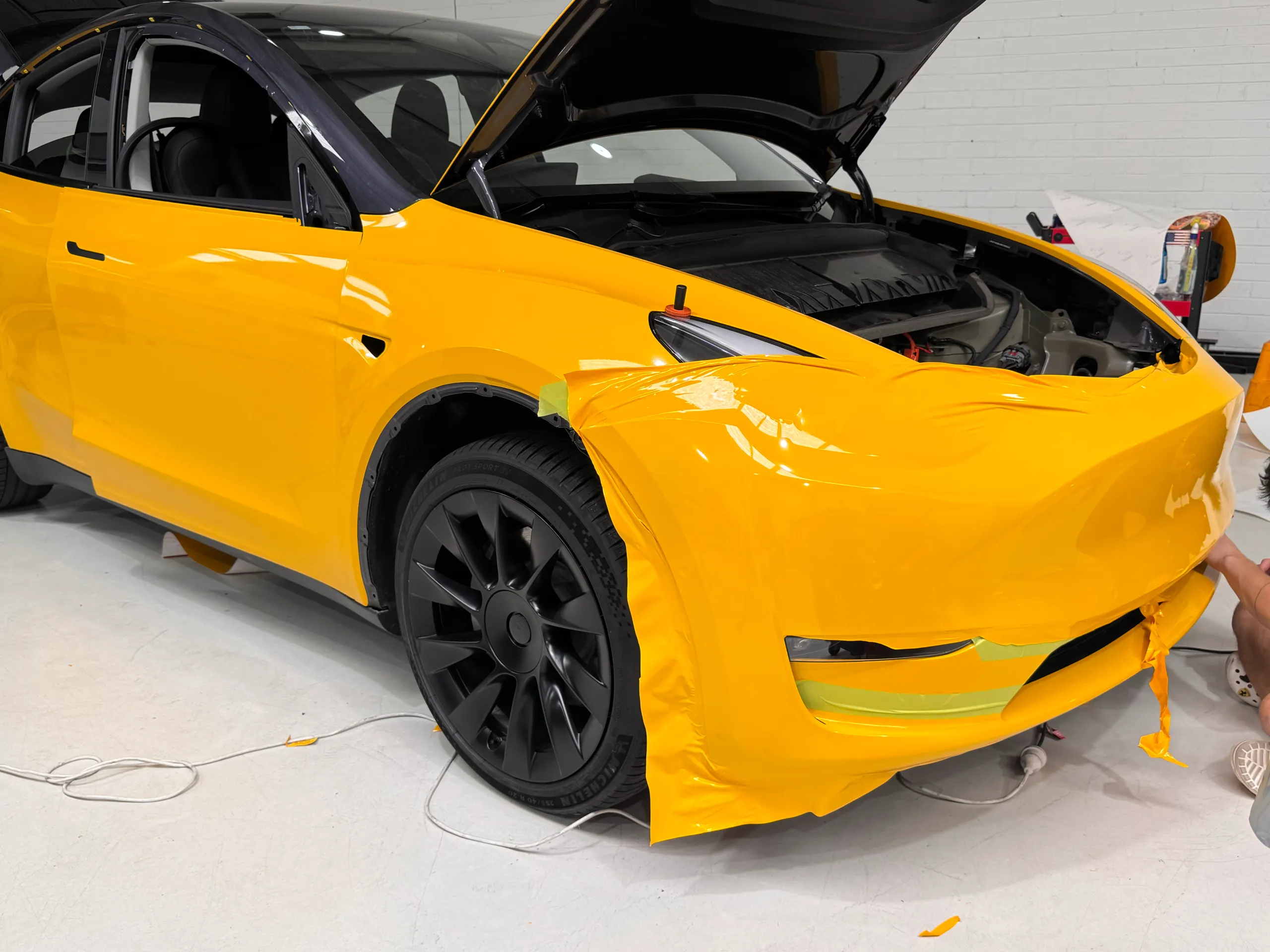 Loose yellow film across the Tesla Model Y front bumper during installation