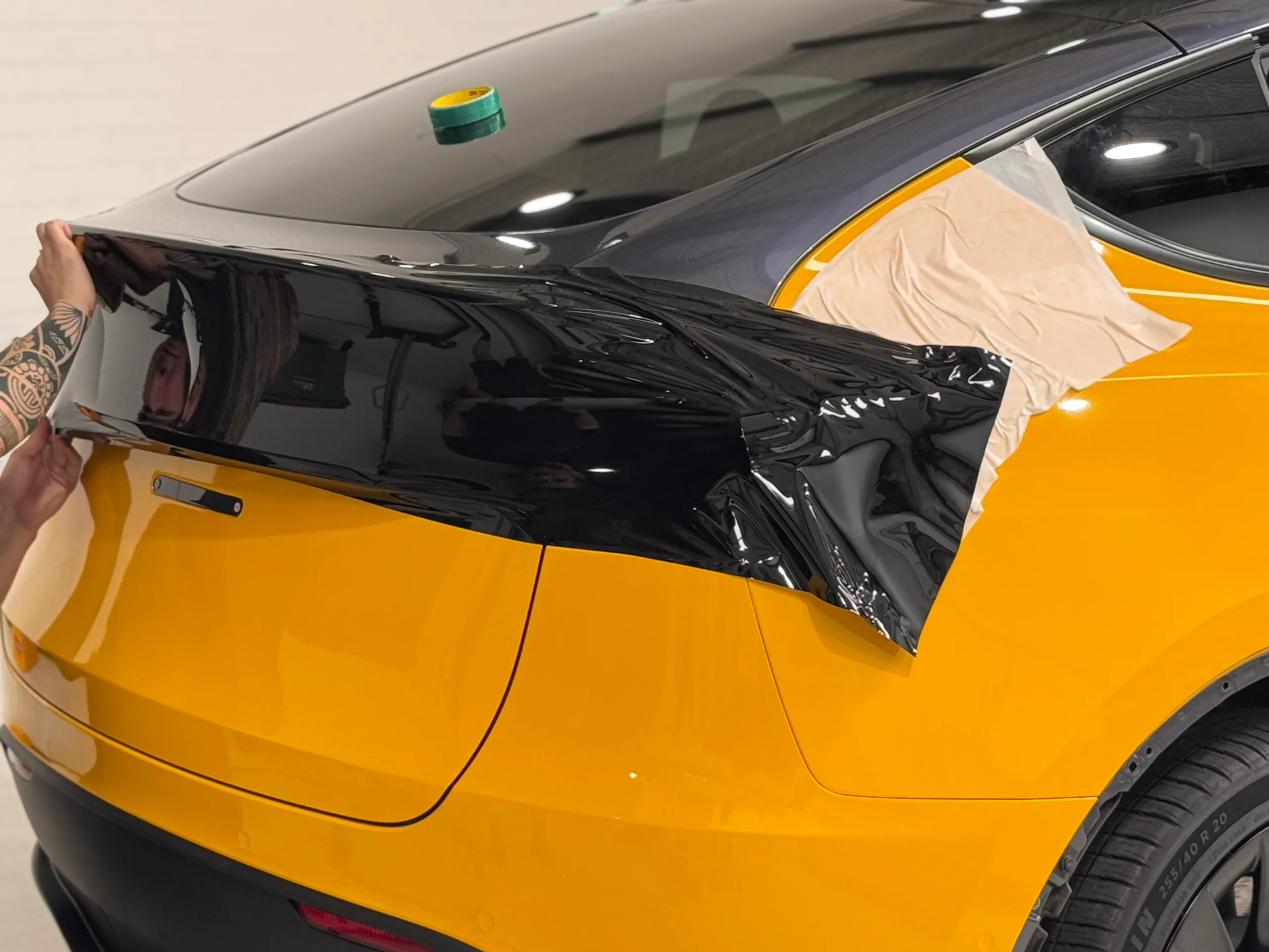 Gloss black film being fitted to the yellow Tesla Model Y upper tailgate
