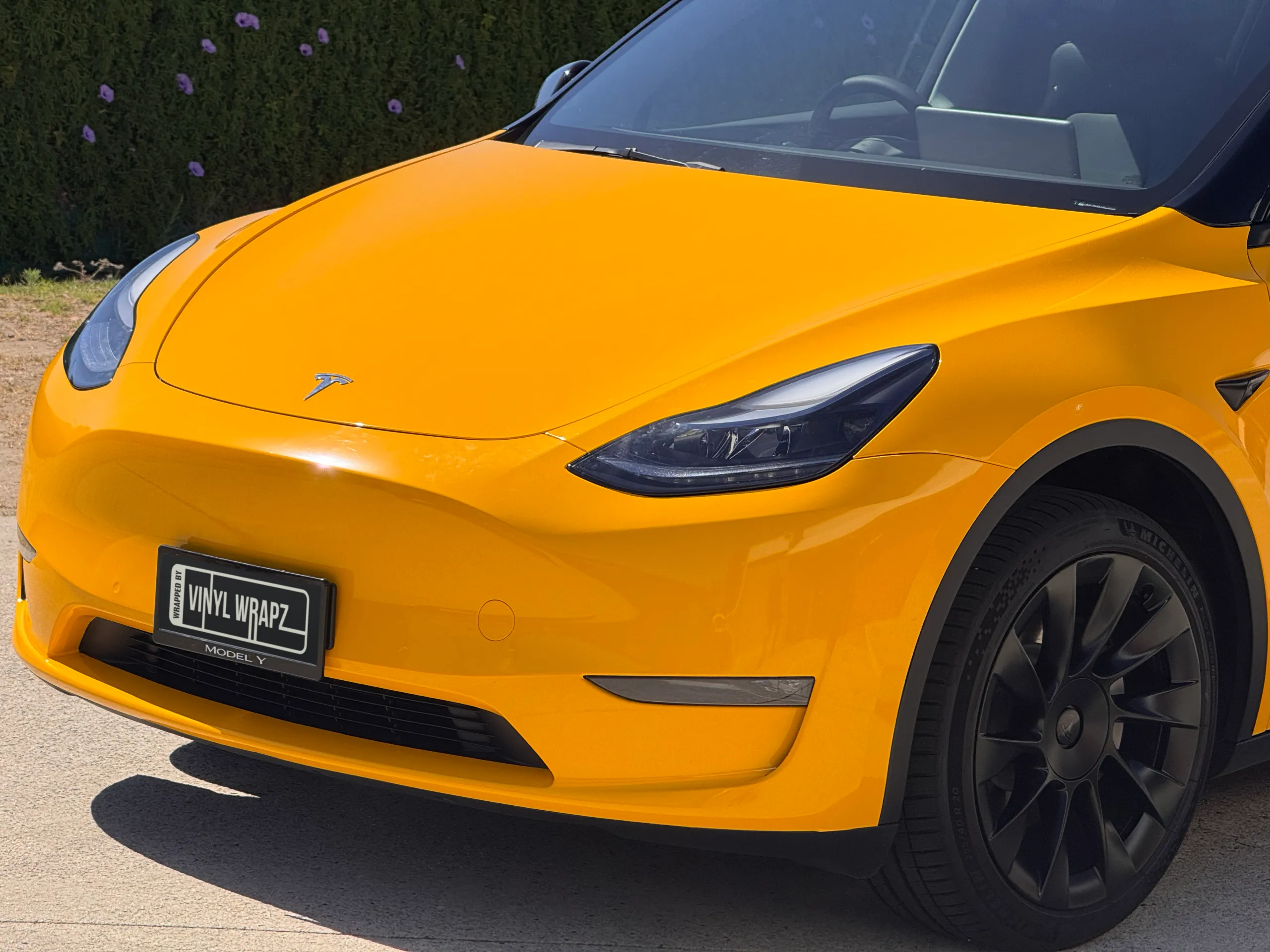 Gloss yellow Tesla Model Y bonnet, headlight and front wheel outdoors
