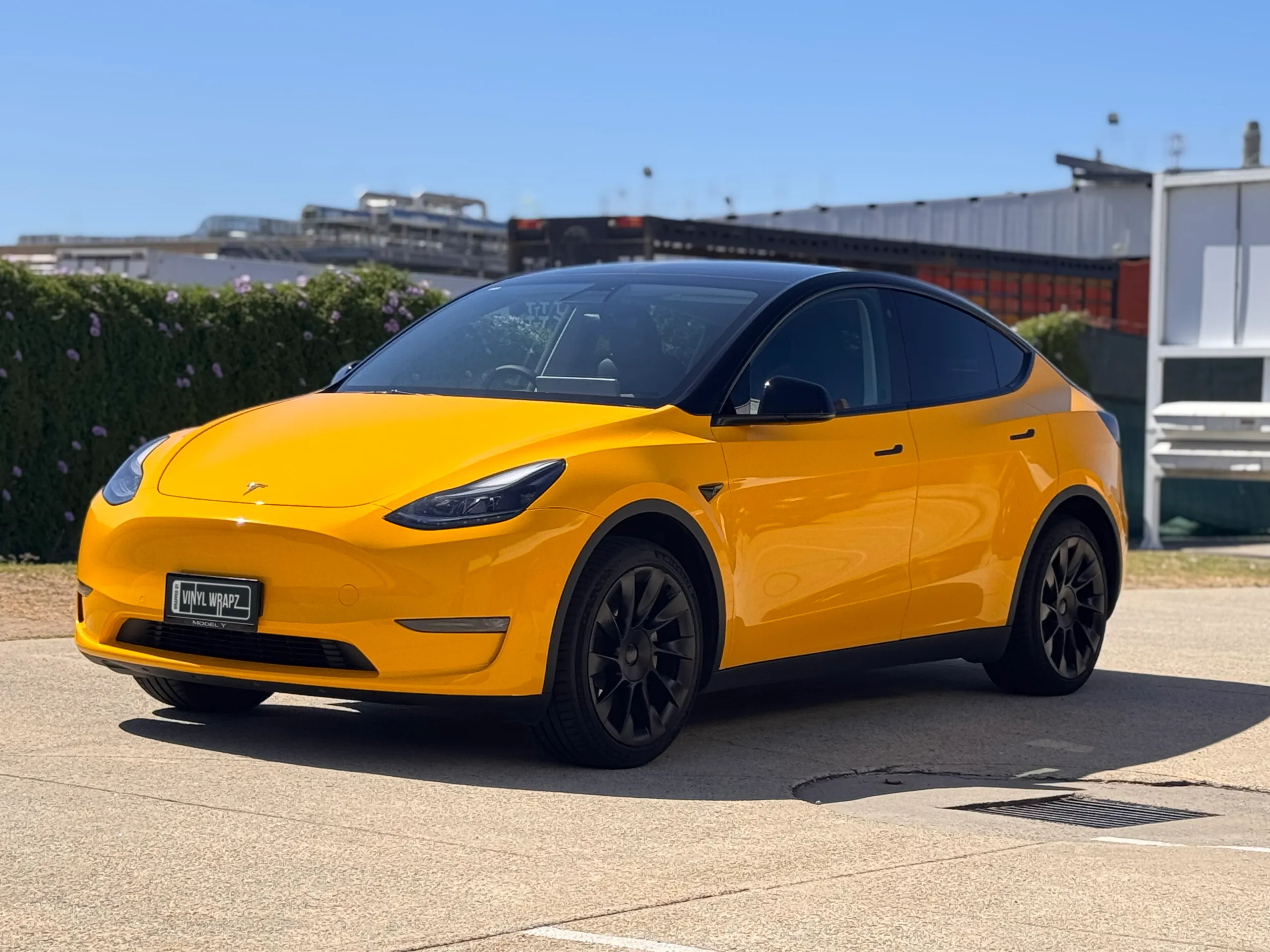 Yellow Tesla Model Y with a black roof and wheels outside the workshop