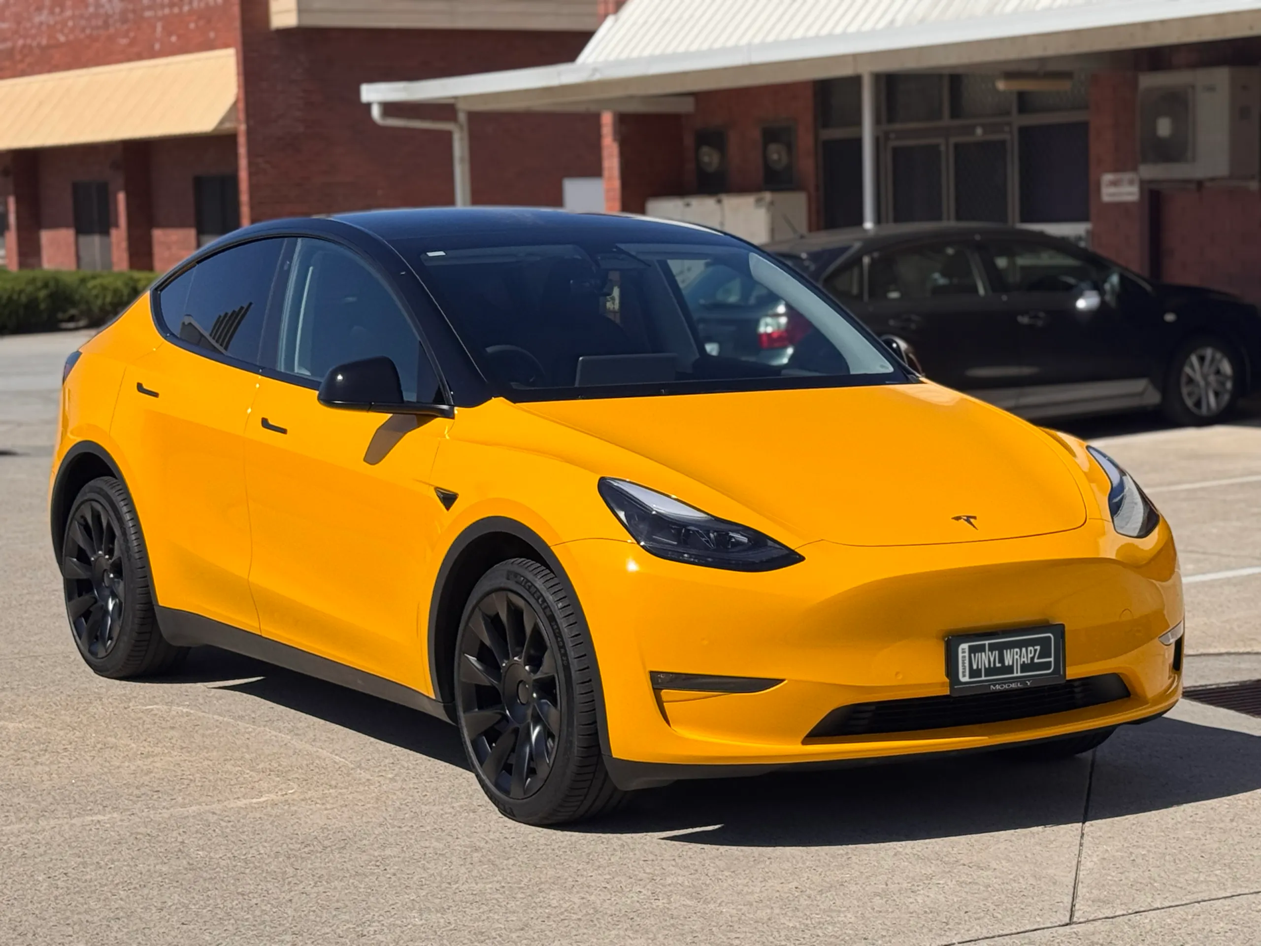 Front-quarter view of the yellow and black Tesla Model Y outside the workshop