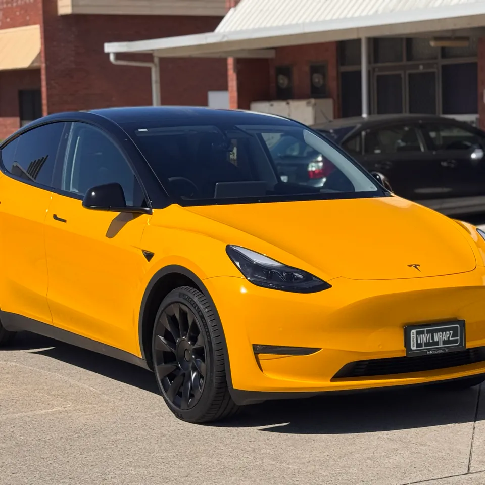 Front-quarter view of the yellow and black Tesla Model Y outside the workshop