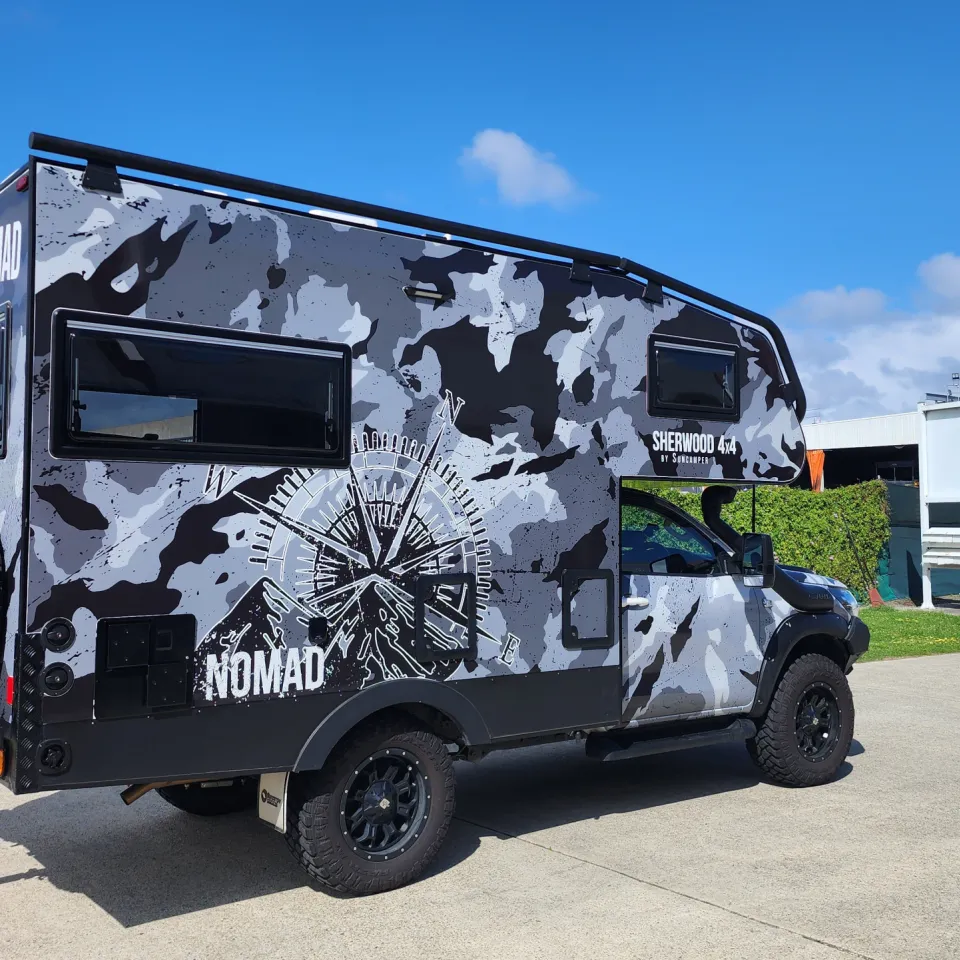 Toyota Hilux Suncamper with grey camouflage, a compass graphic and NOMAD lettering outdoors