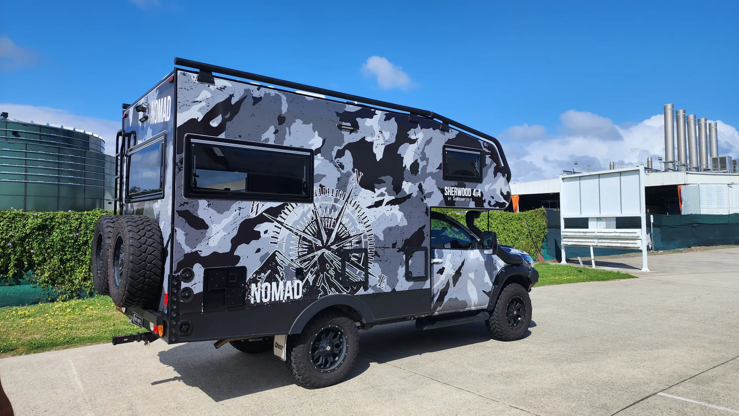 Toyota Hilux Suncamper with grey camouflage, a compass graphic and NOMAD lettering outdoors