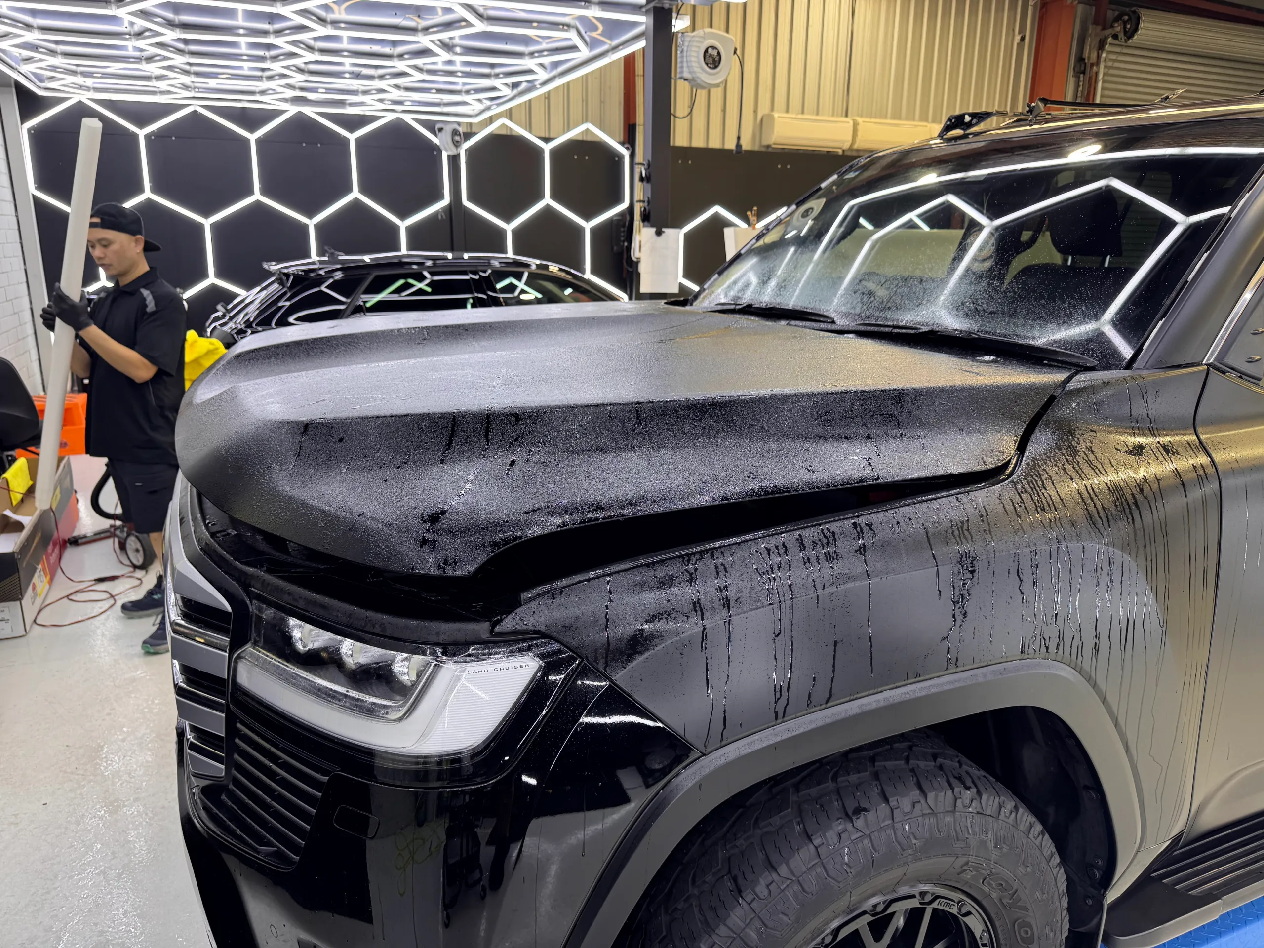 Wet LandCruiser bonnet during preparation, with an installer beside the vehicle